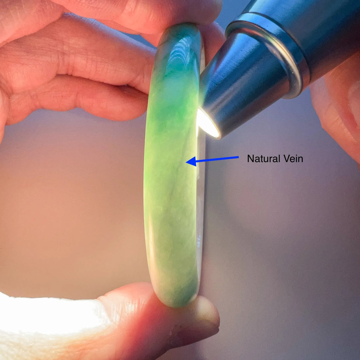 Side view of translucent green-white jadeite bangle backlit to reveal its natural vein and smooth polished finish