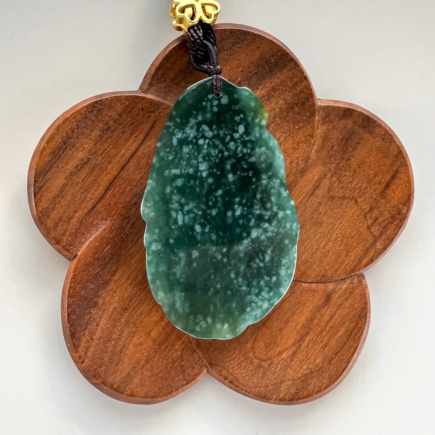 Back view of green jade pendant on petal-shaped wood stand, smooth polished surface