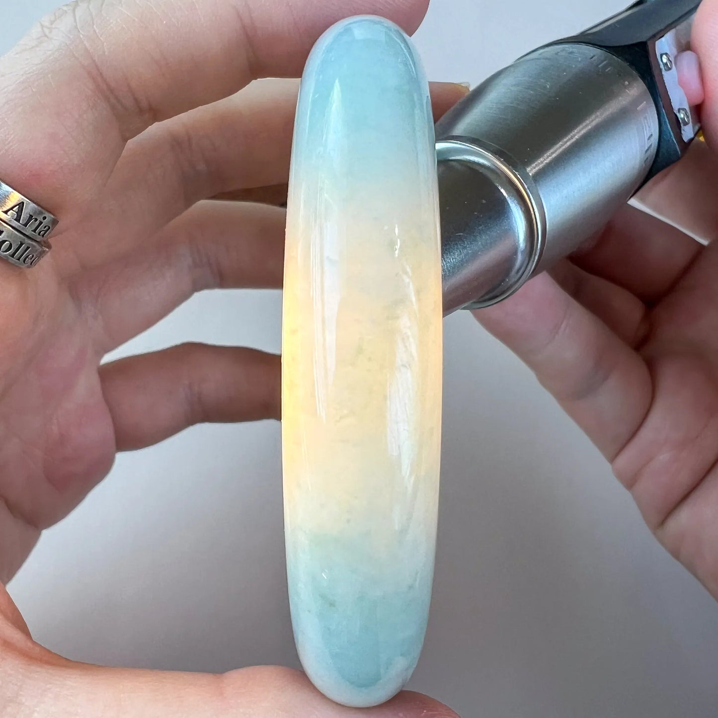 Backlit side view of pale jade bangle highlighting milky translucence and soft blue tones