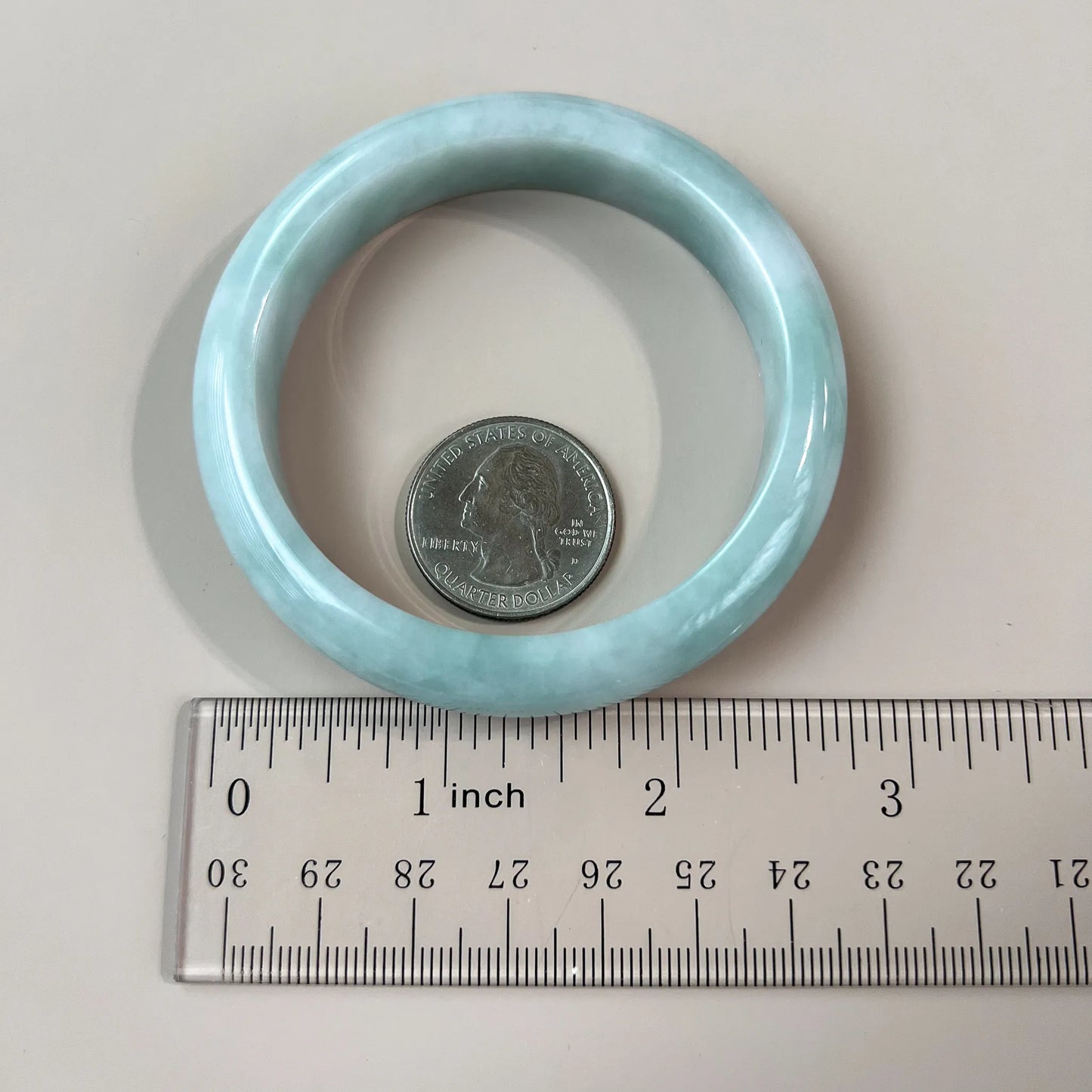 Light green blue jadeite bangle shown top-down with quarter and ruler for size, polished smooth finish, translucent texture