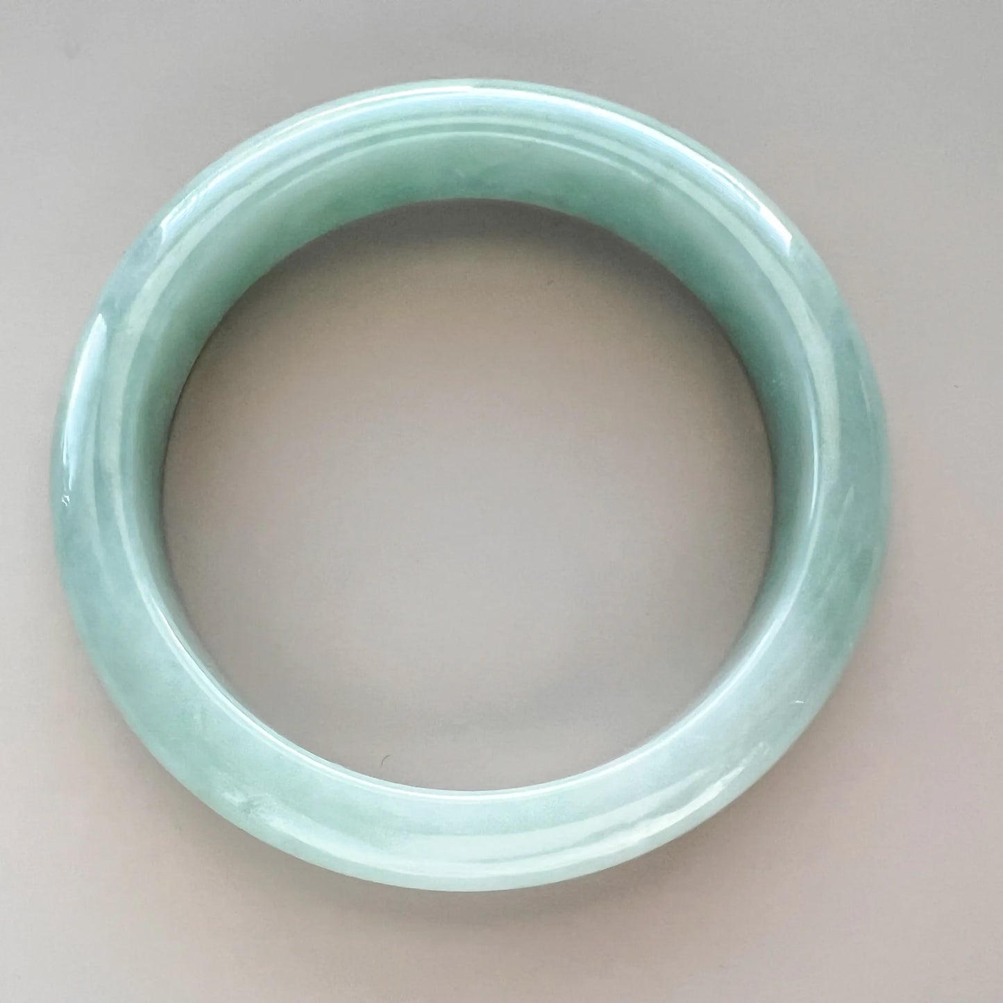 Top-down view of light green jadeite jade bangle with smooth glossy finish and translucent Burmese-style texture