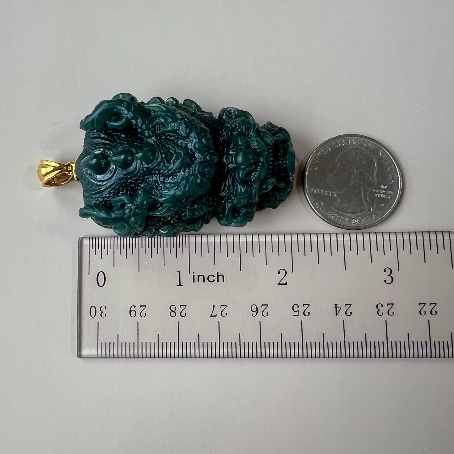 Side view of carved green jade pendant with ruler and quarter for scale