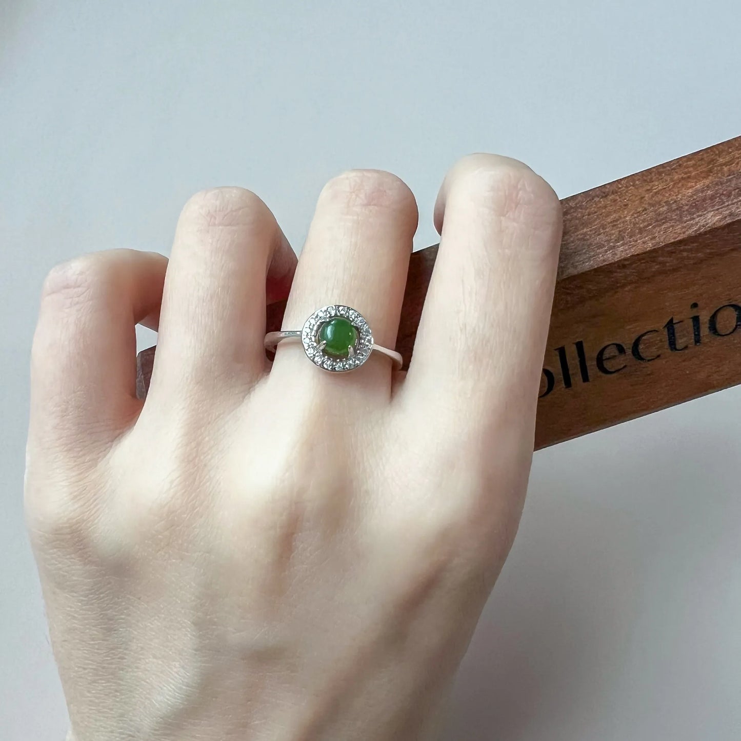 Ring worn on hand showing polished silver band and round green gemstone setting