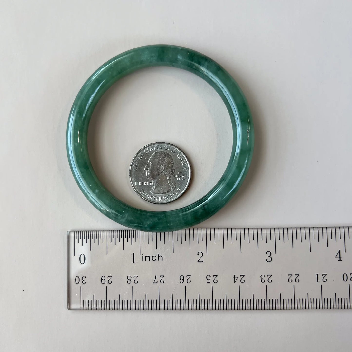 Green jade bangle shown with quarter and ruler for scale