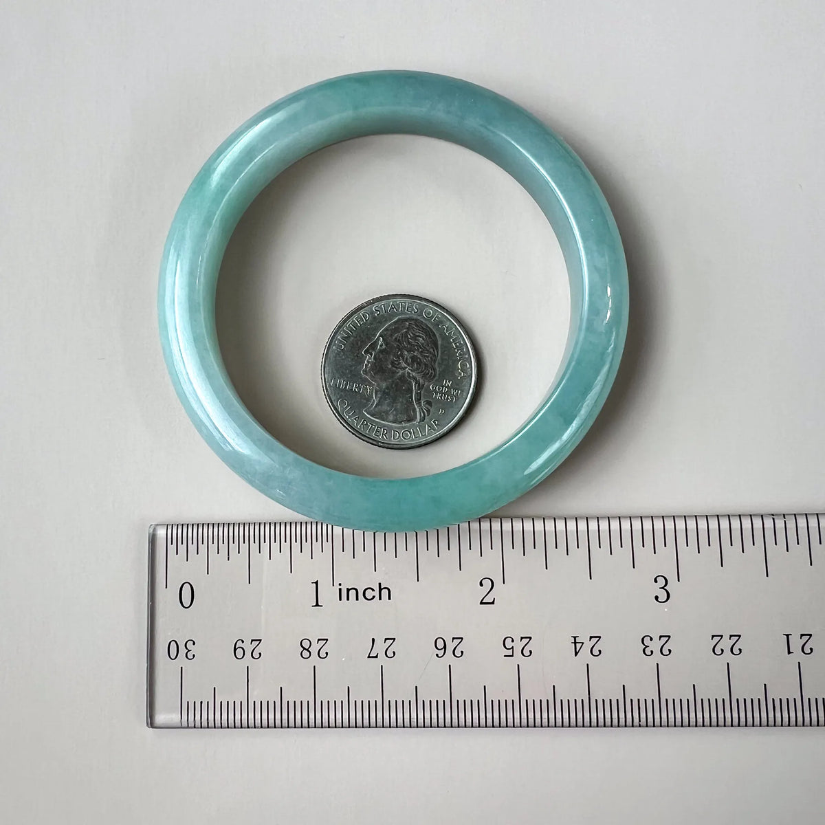 Light green-blue jadeite bangle shown beside a ruler and quarter for size and scale