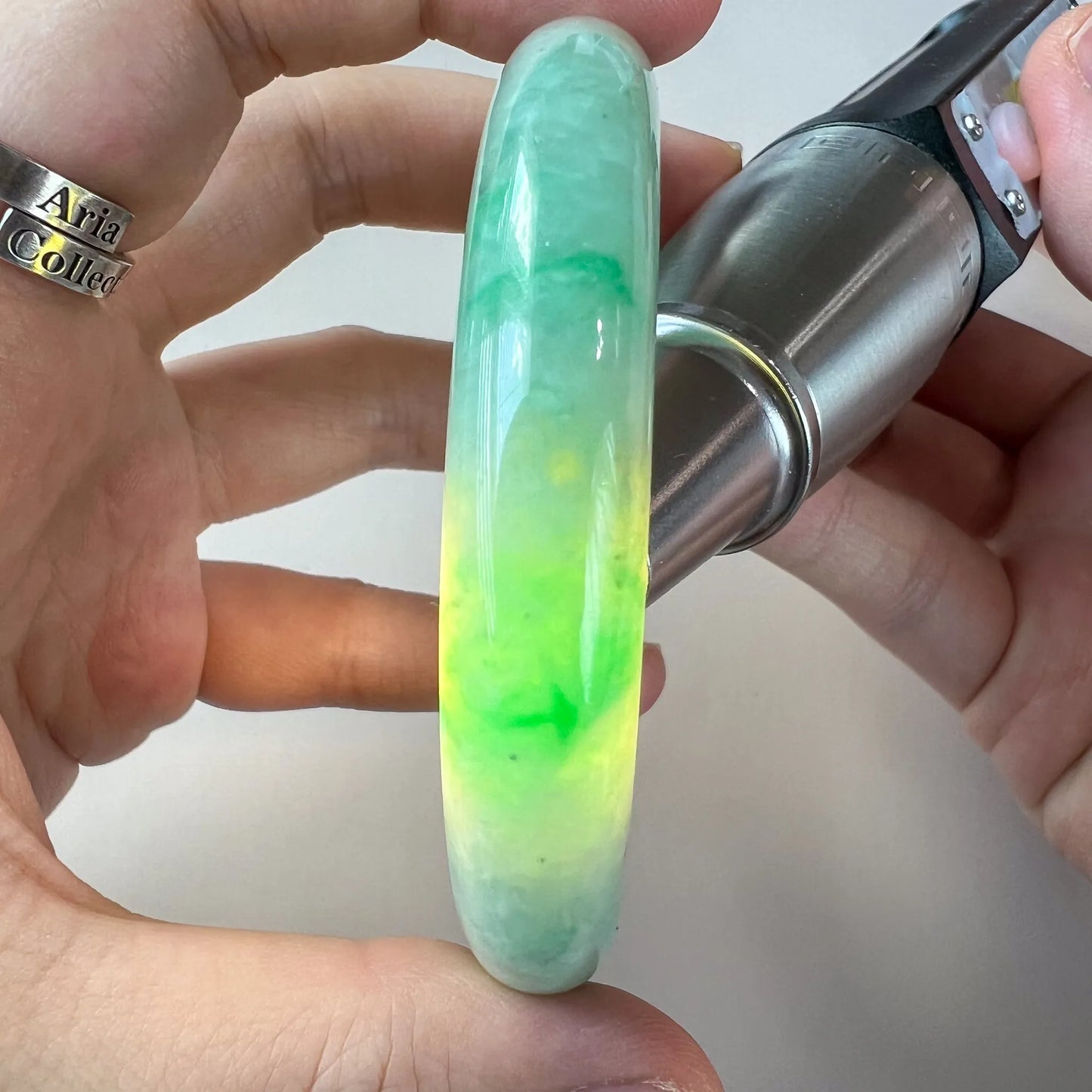 Side profile of jade bangle held in hand under bright light, revealing vivid green translucence
