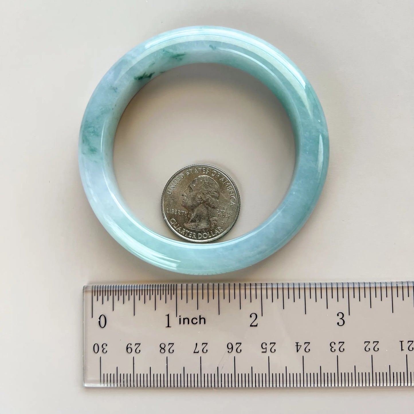 Blue-green jadeite bangle shown flat beside a ruler and quarter for scale