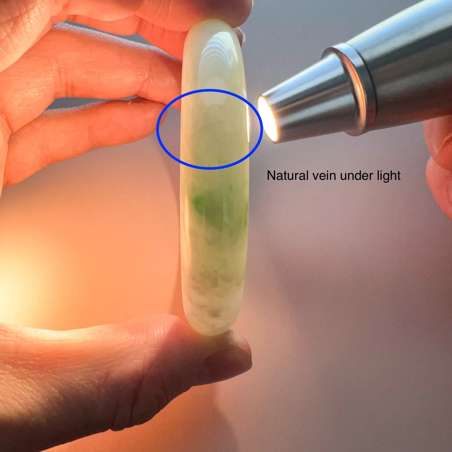 Light green jadeite bangle held under a flashlight, showing translucent polished finish and natural veining detail
