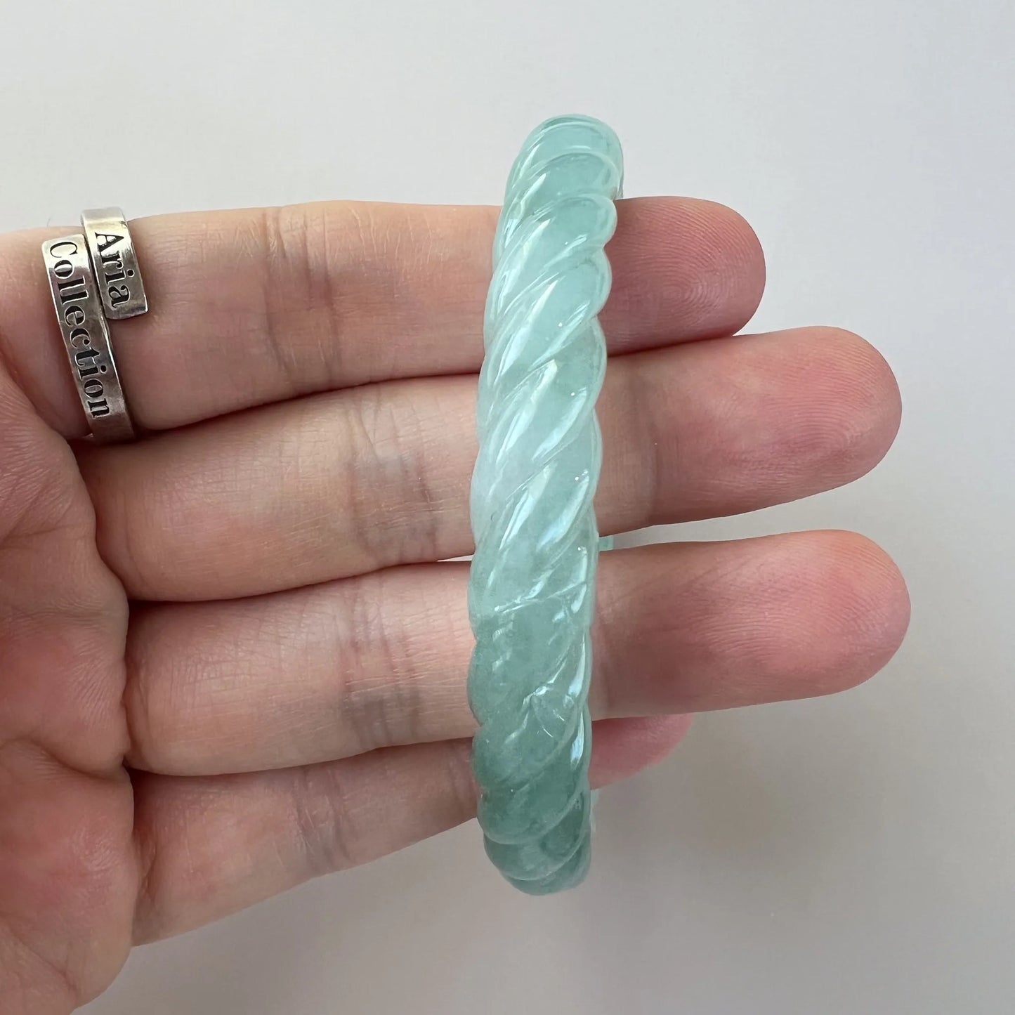 Side view of mint green carved jade bangle, glossy twisted finish, hand-held close-up