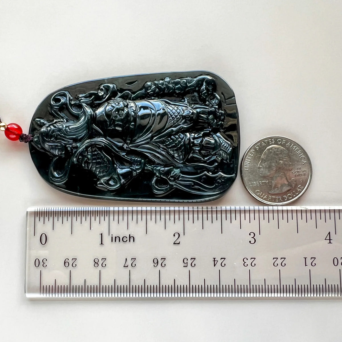 Pendant laid flat with ruler and coin for size reference, showing glossy carved black stone
