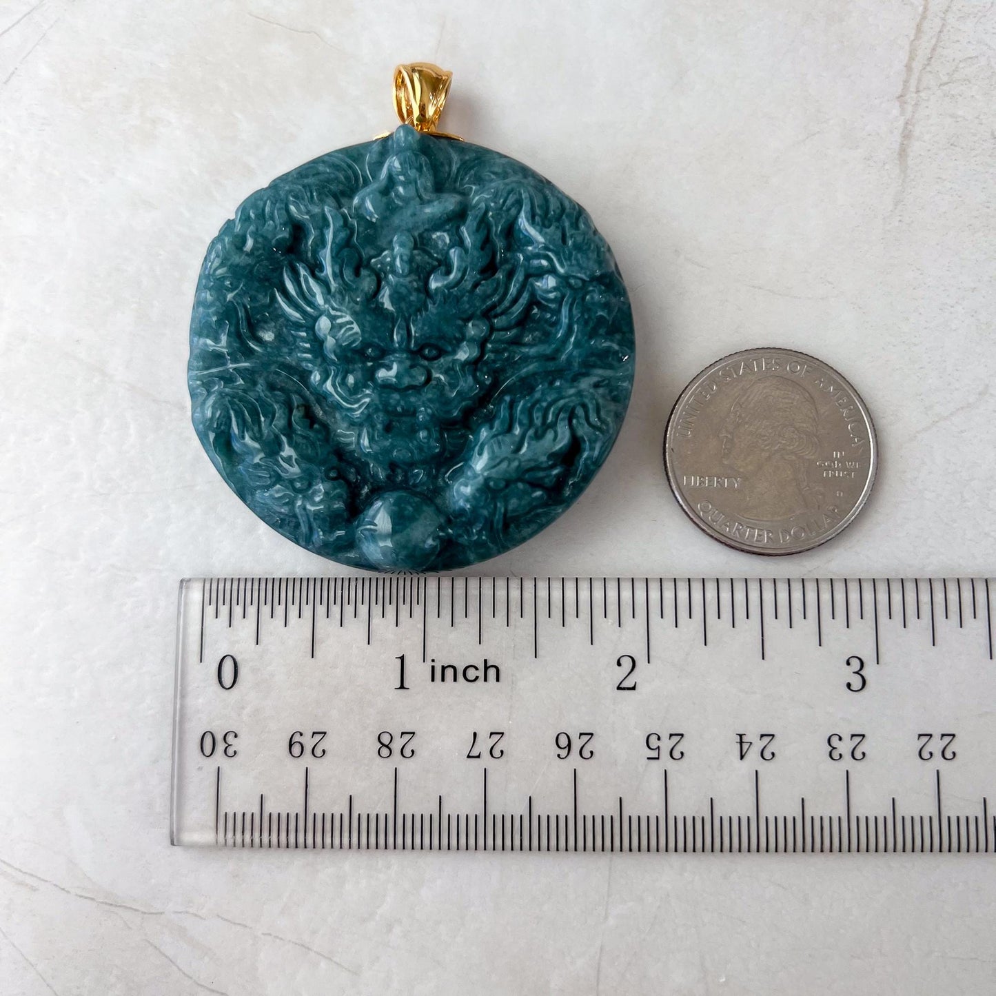 Top-view green jadeite pendant with dual-sided dragon carving, glossy finish, and 18K gold bail beside ruler and quarter