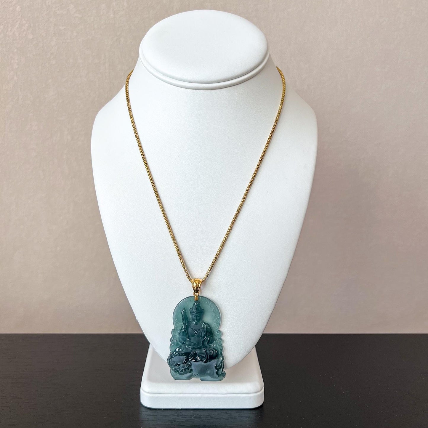 Front view of jadeite Manjushri Buddha pendant with 18K gold bail on gold chain, displayed on white bust stand
