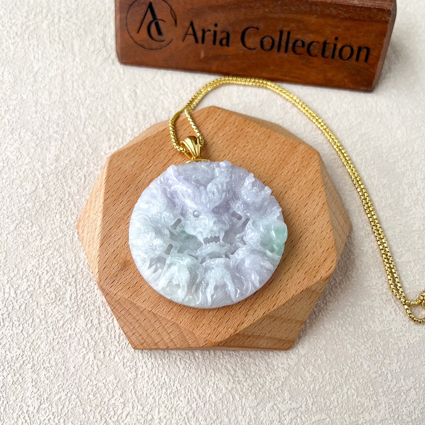 Light purple jadeite pendant with dual-sided carved texture and 18K gold bail on a gold chain, displayed on wood stand