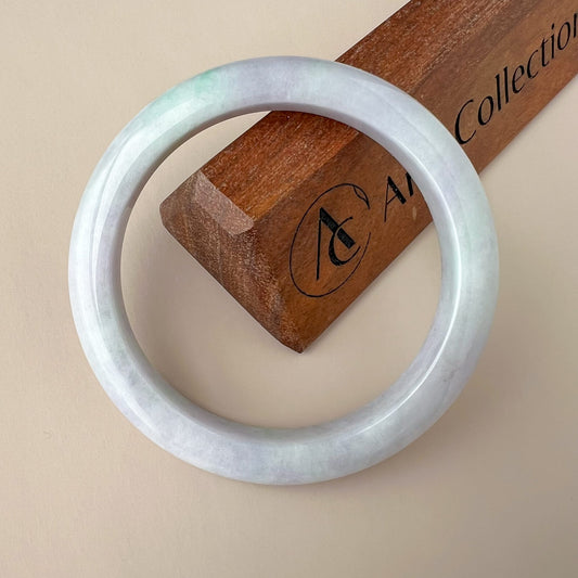 Light lavender and green Burmese jadeite bangle angled on a wooden display stand, smooth polished finish, 57.6 mm