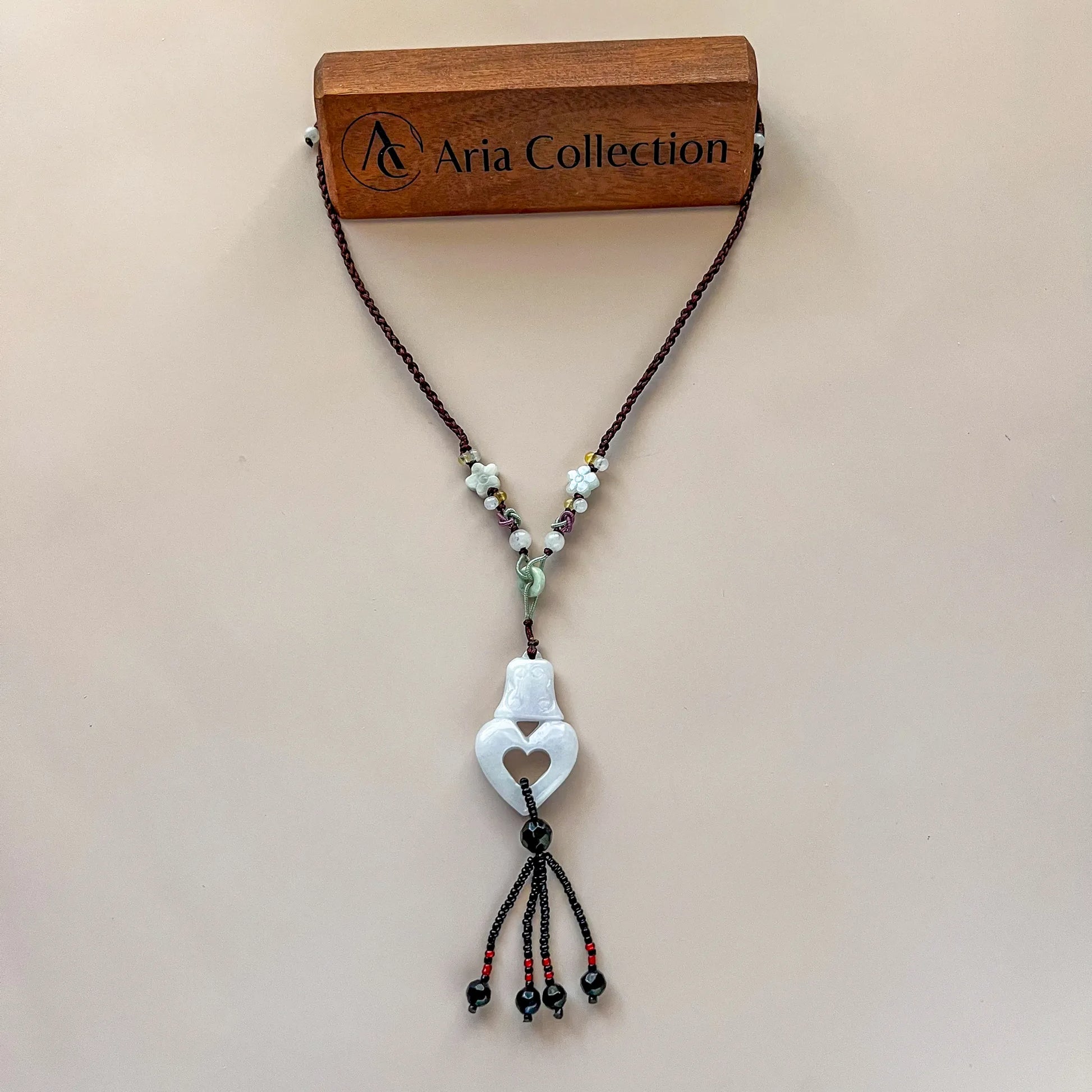 Hand-carved white jade heart pendant necklace with lavender braided cord, floral beads, and tassel on display card