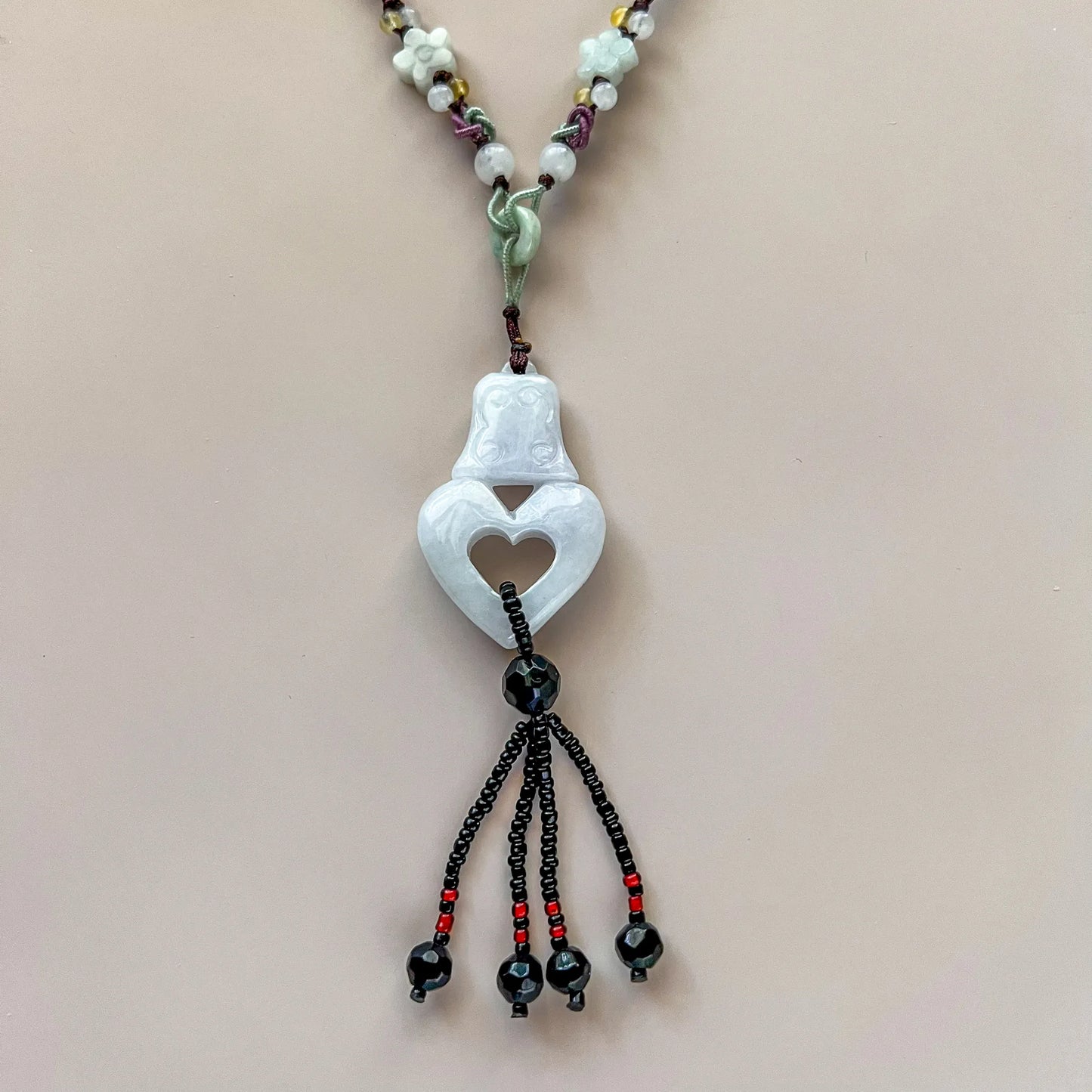 Front view of hand-carved white jadeite pendant necklace with heart cutout, beaded cord, and tassel detail