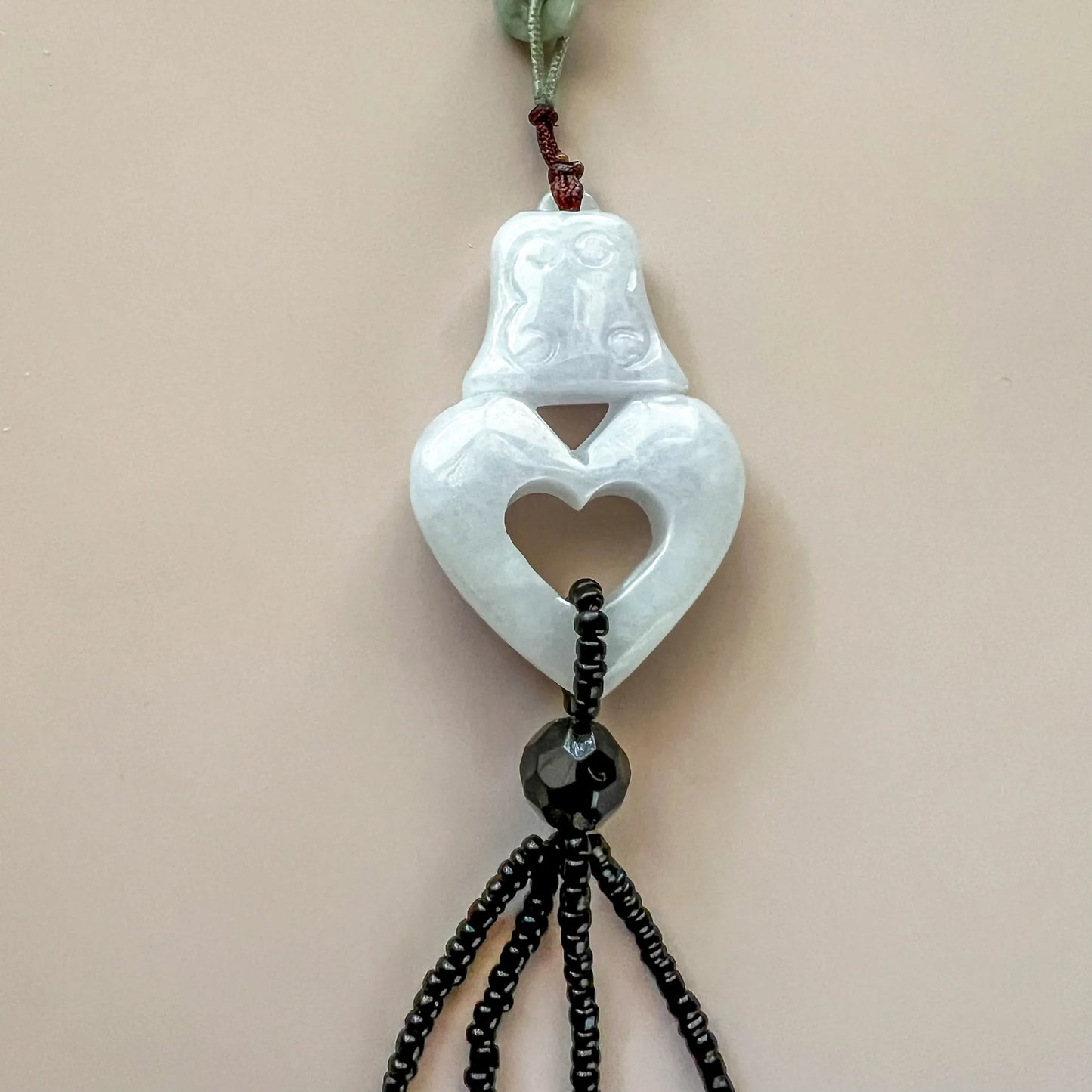 Hand-carved white lavender jadeite pendant necklace with heart cutout and beaded black cord, close-up front view