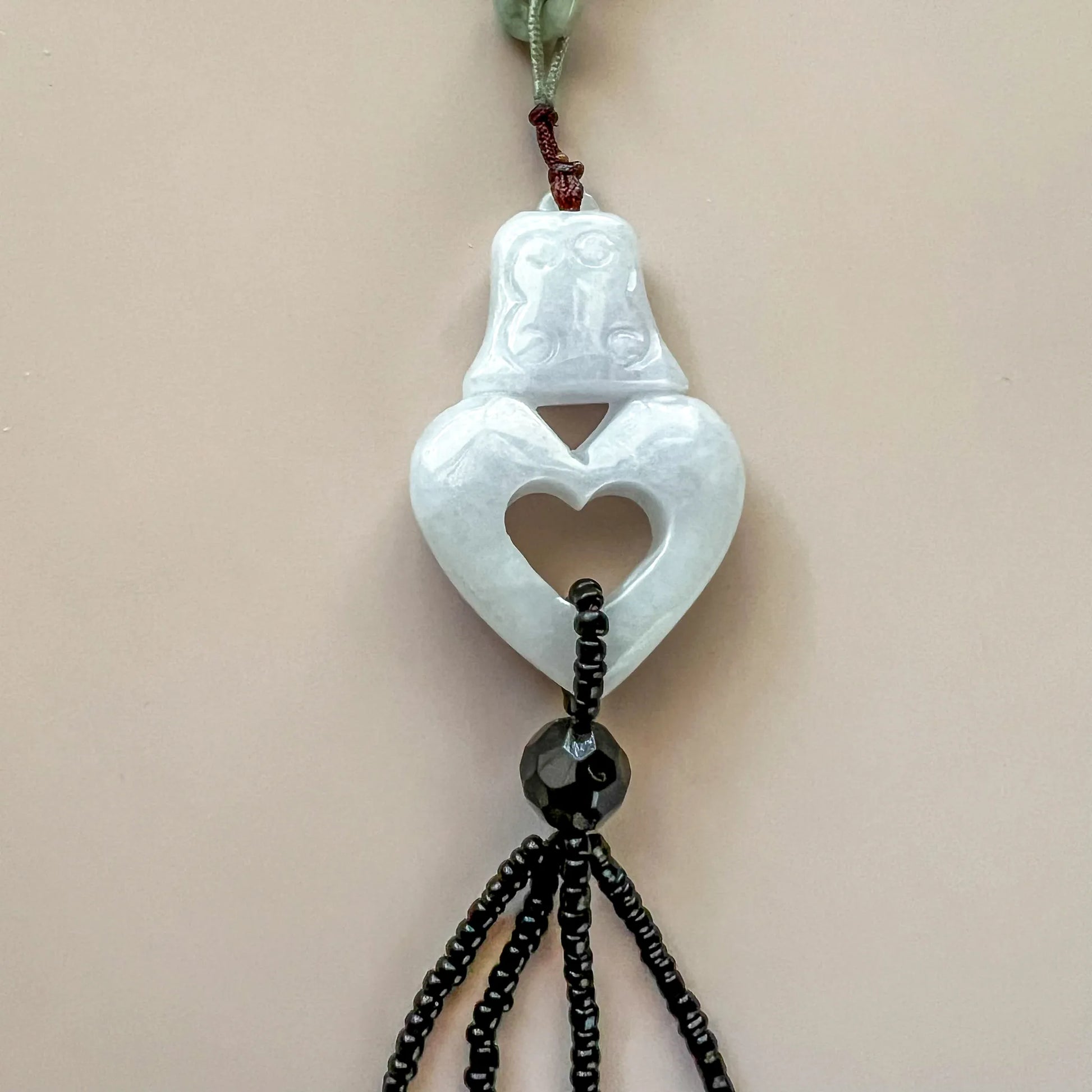 Hand-carved white lavender jadeite pendant necklace with heart cutout and beaded black cord, close-up front view