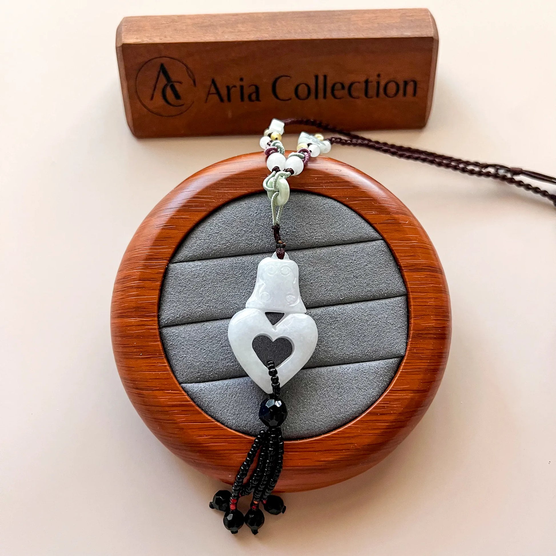 Hand-carved white lavender jadeite pendant necklace on wooden display, heart cutout, beaded cord, close-up angle