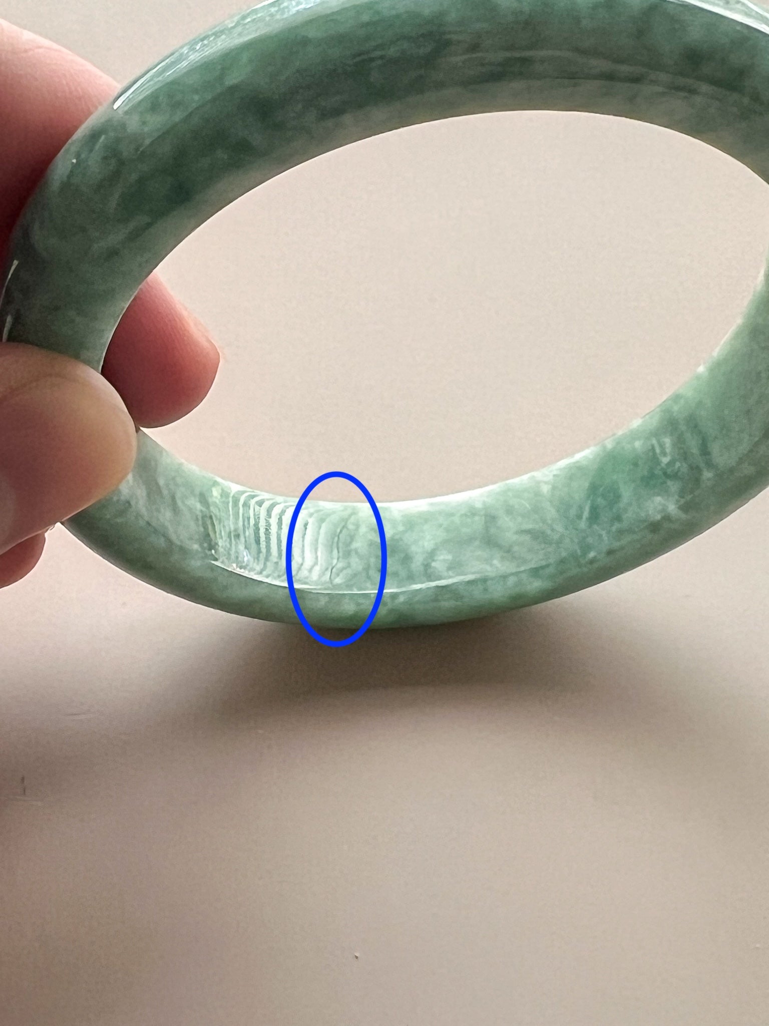 Close-up angled view of mottled green jadeite bangle with polished finish and visible natural texture flaw highlighted in blu