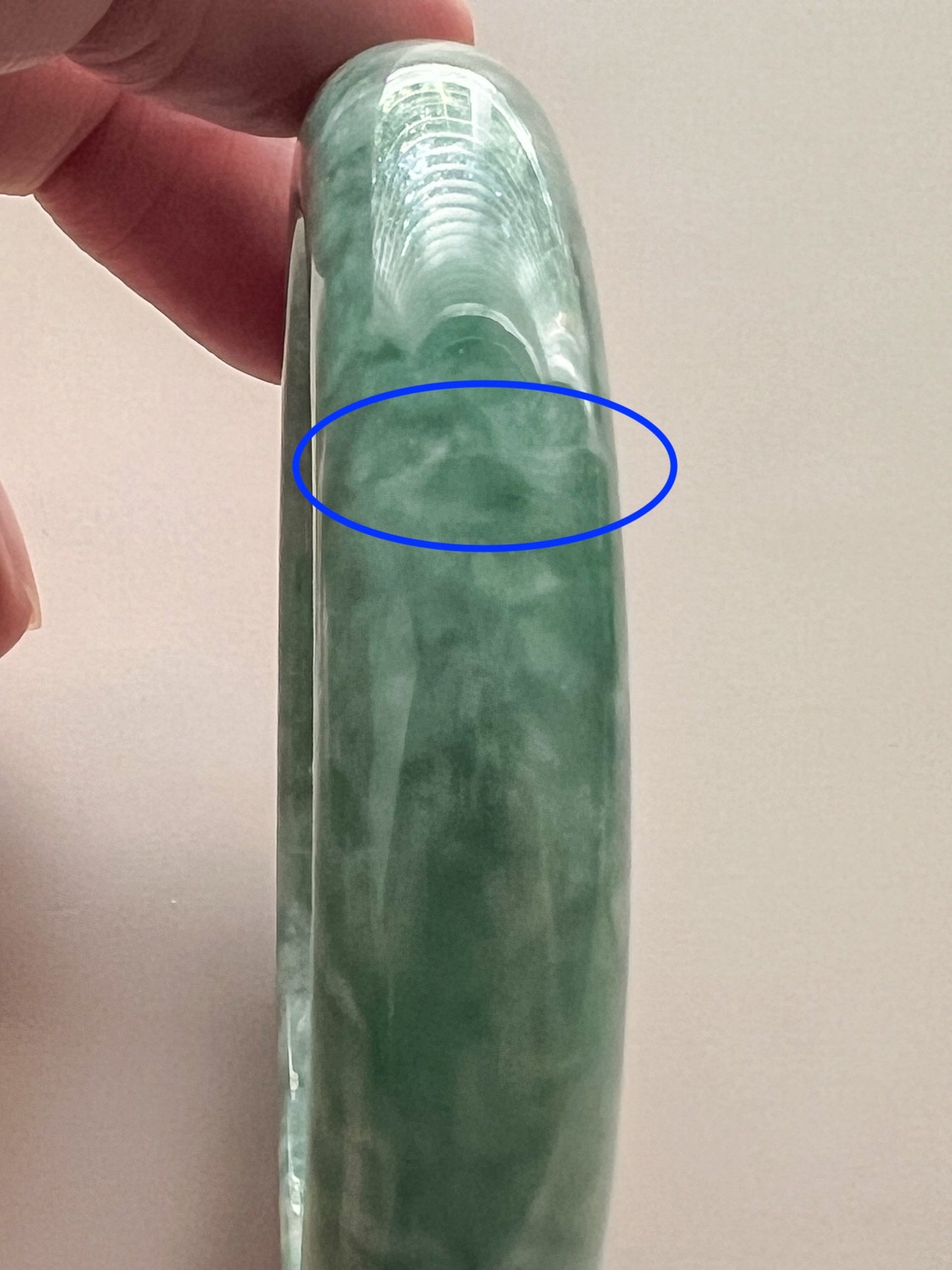 Side view of mottled green jadeite bangle with glossy polished finish and visible cloudy inclusion area highlighted in blue