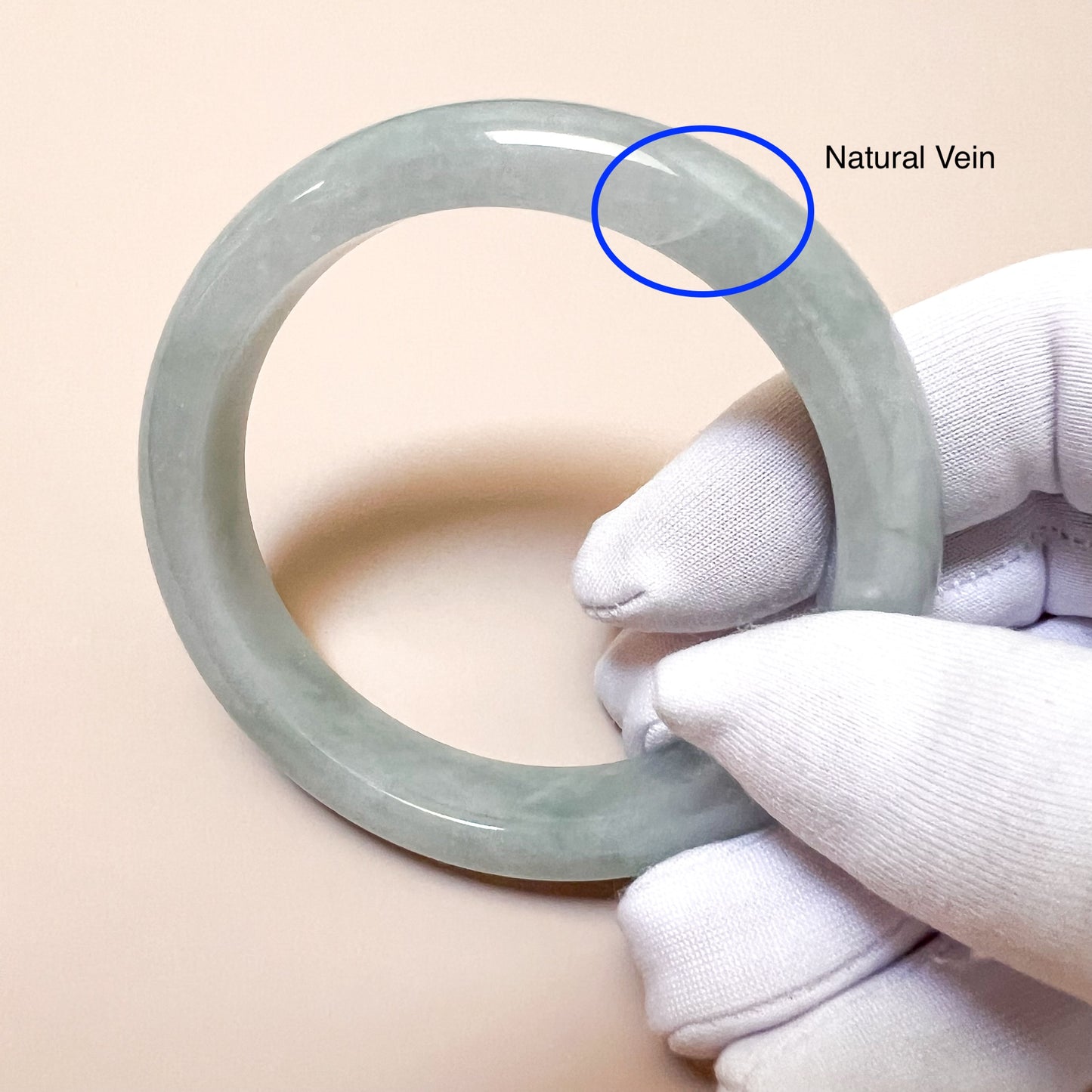Light green gray jadeite bangle held at an angle, glossy polished finish with visible natural vein detail
