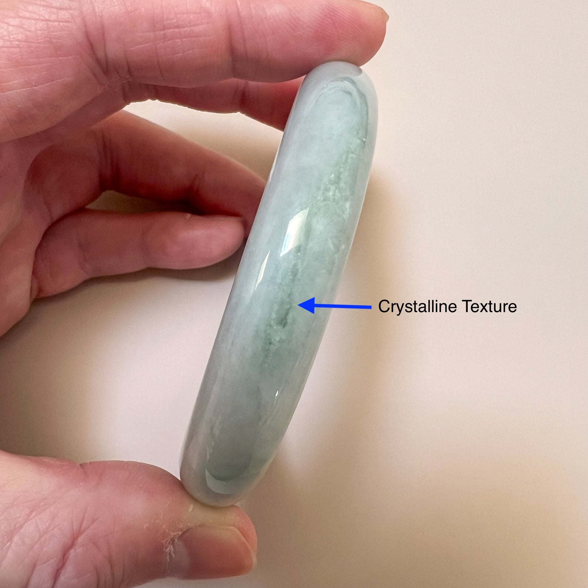 Close-up side view of a light green gray jadeite jade bangle with polished finish and crystalline texture detail