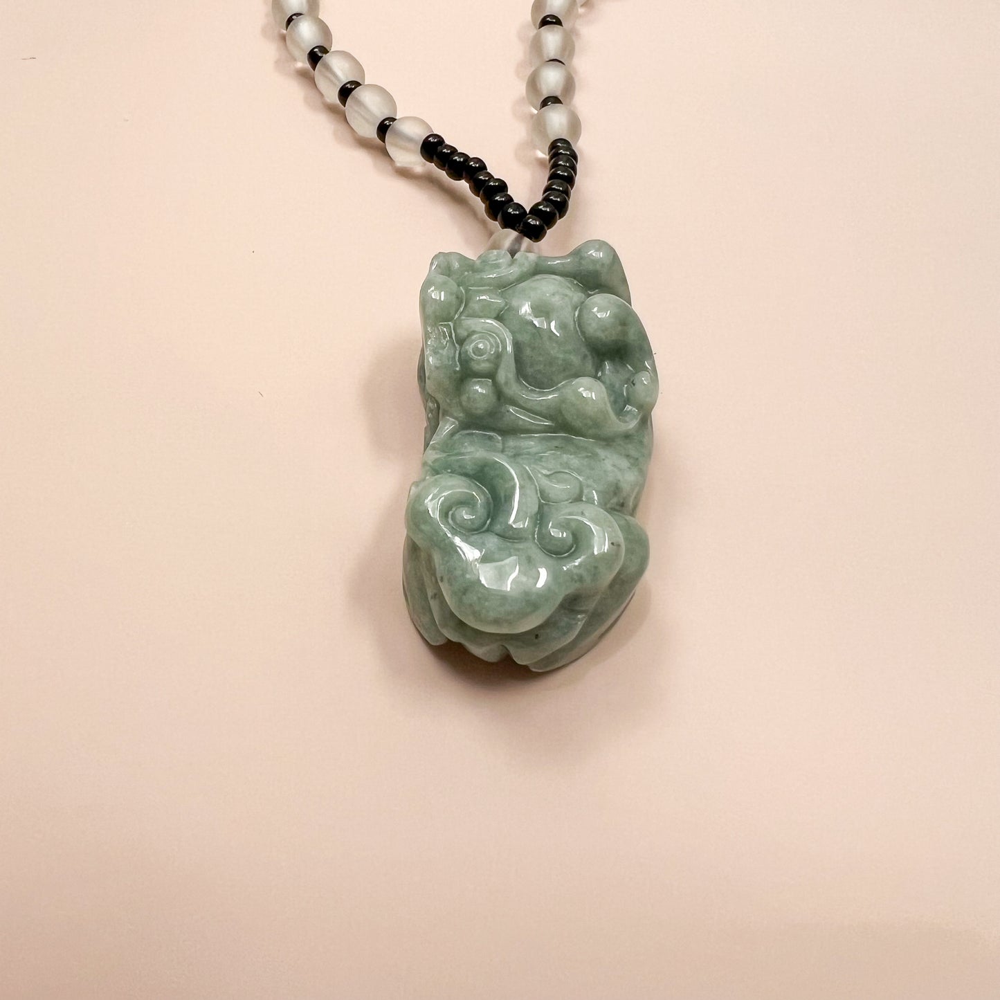 Close-up of green jadeite Pixiu pendant necklace with polished carved texture and black-white beaded cord