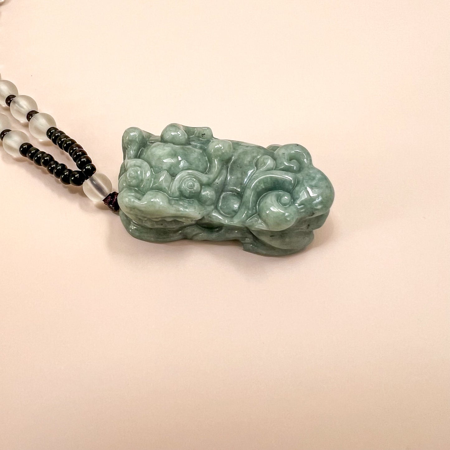 Close-up angled view of green jadeite Pixiu pendant necklace with glossy carved texture and black-white beads