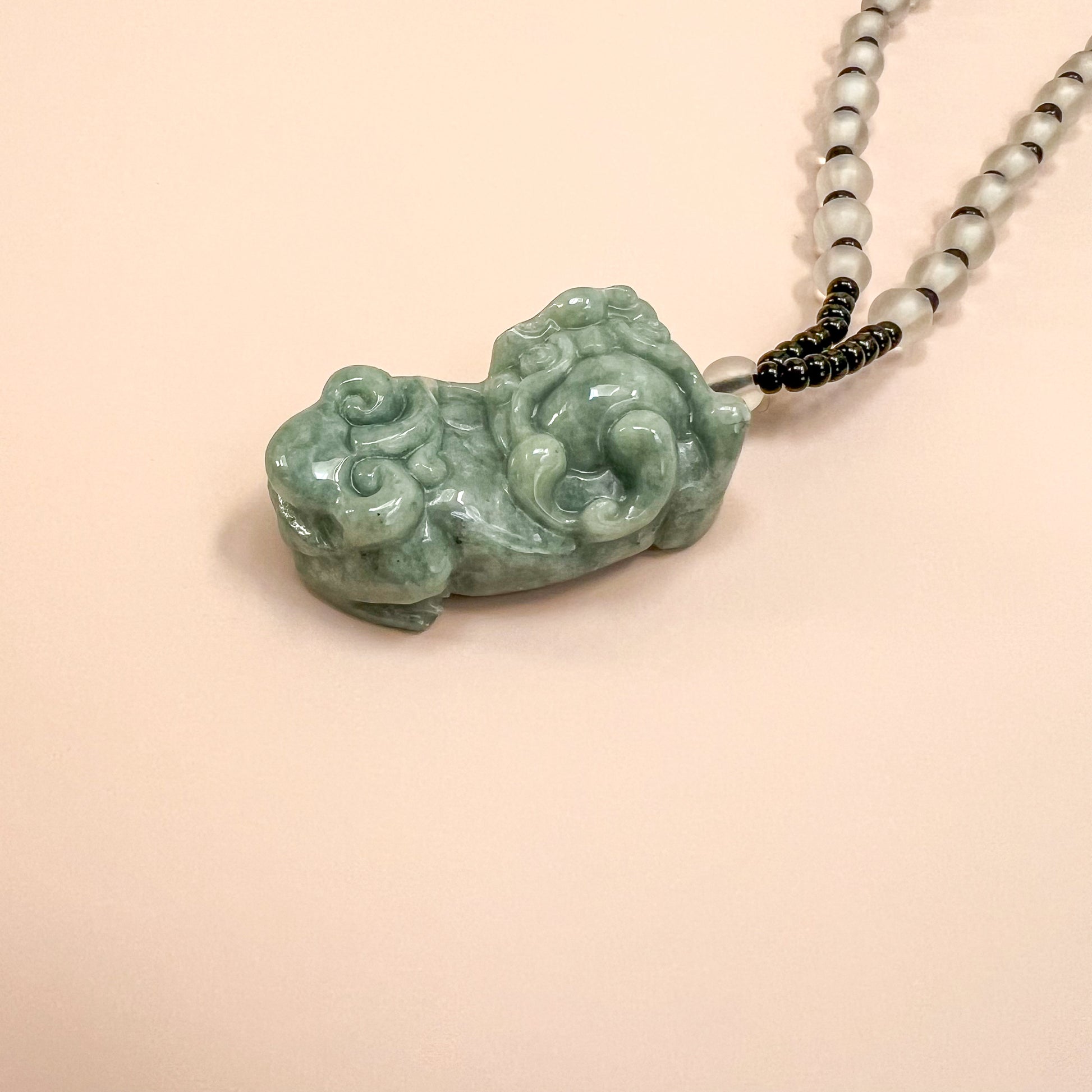 Close-up angled view of green jadeite Pixiu pendant necklace with glossy carved texture and bead strand detail