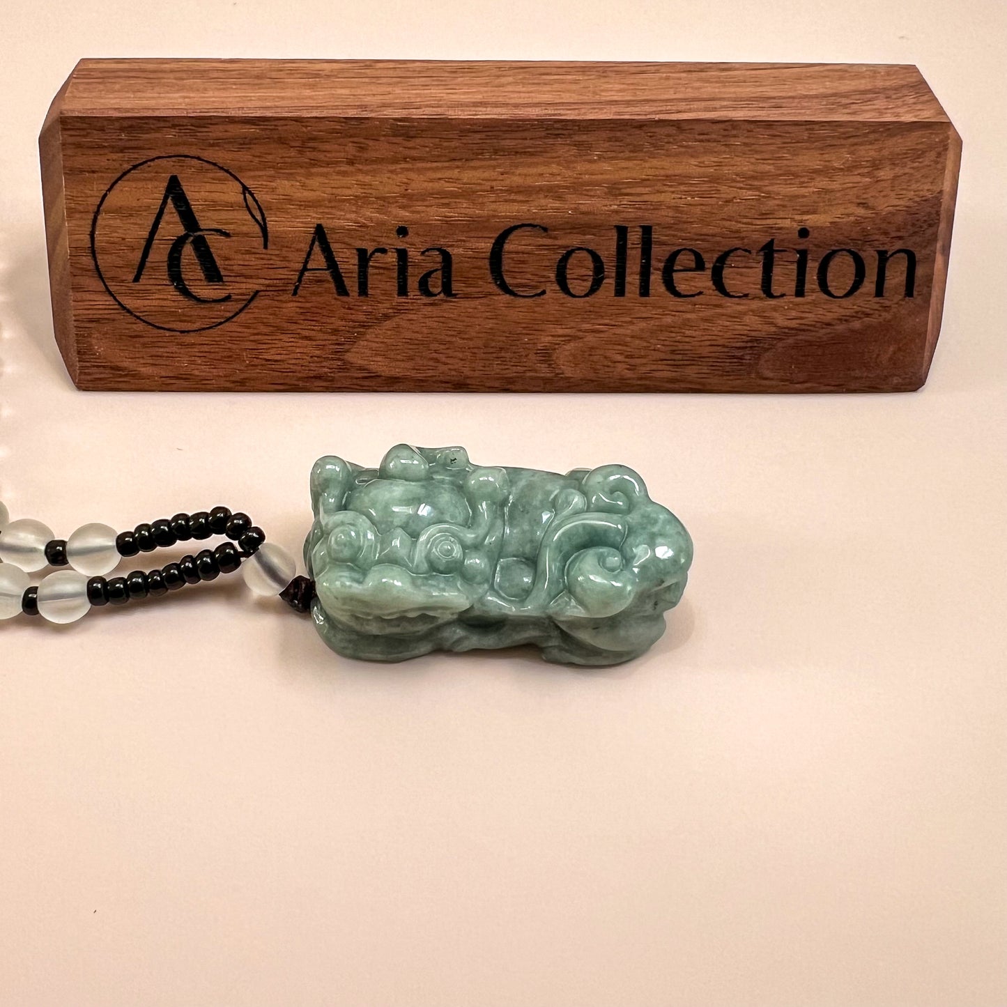 Green jadeite Pixiu pendant necklace with glossy carved texture, shown beneath a wooden display plaque on a white background