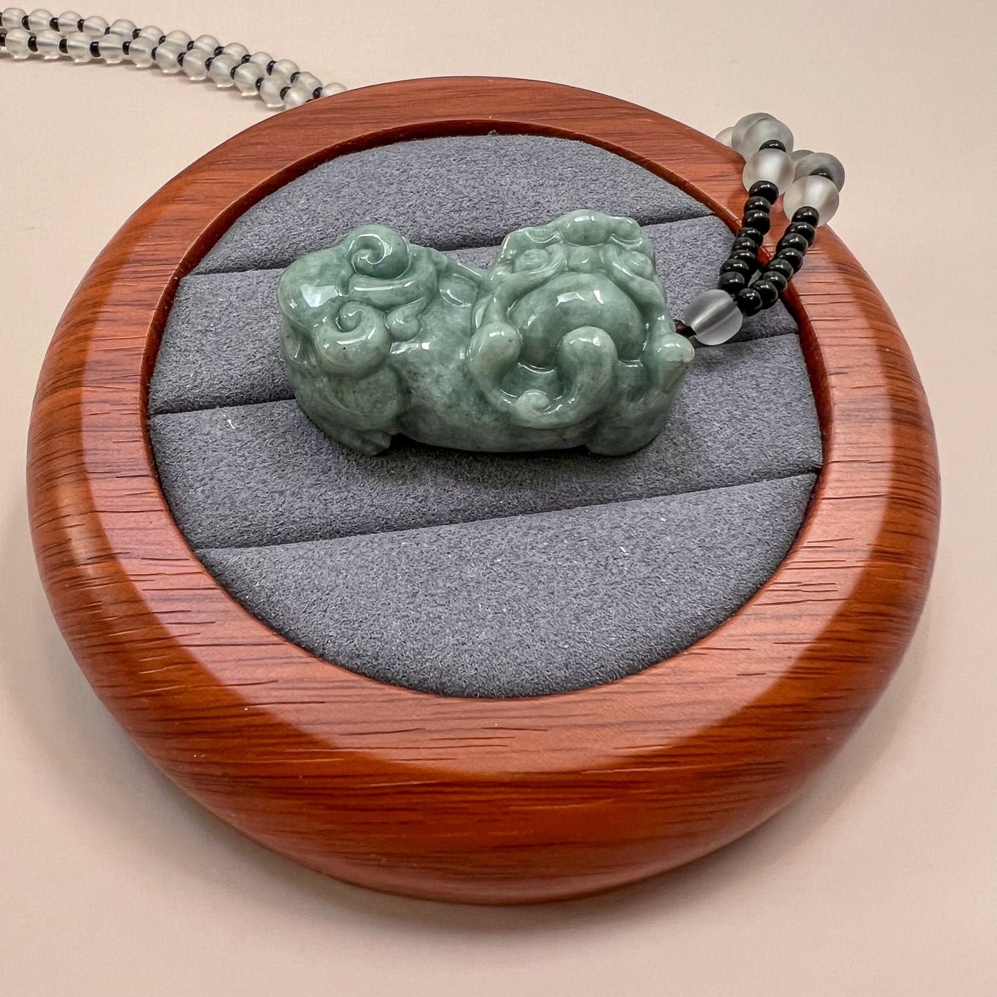 Top view of green jadeite Pixiu pendant necklace in a wooden display tray with gray velvet lining, glossy carved finish