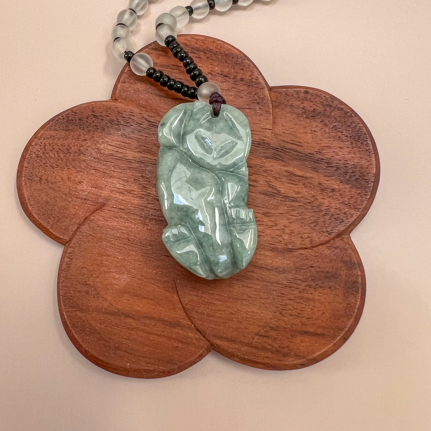 Close-up of green jadeite Pixiu pendant necklace with glossy carved finish on beaded cord over wooden display