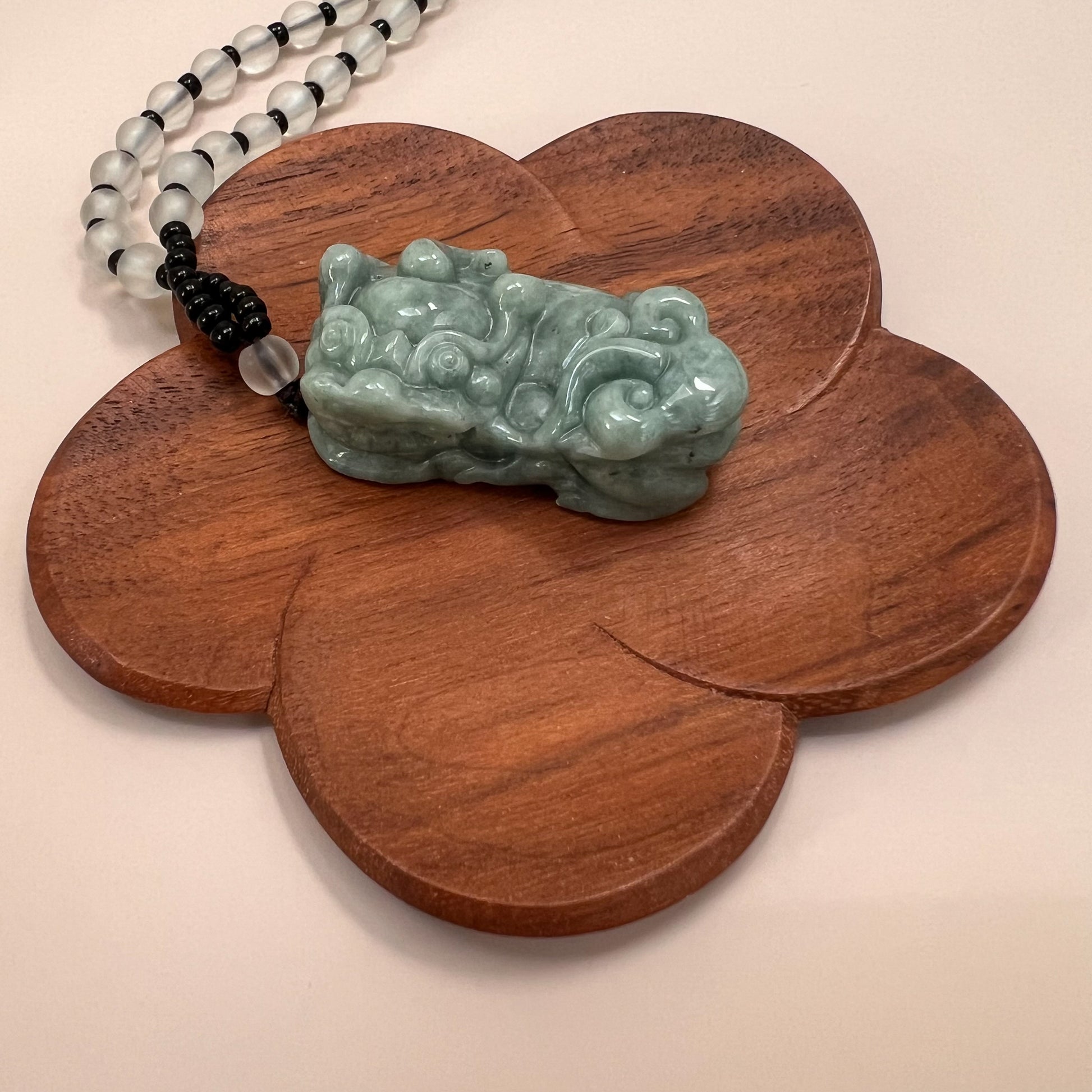 Green jadeite Pixiu pendant necklace on carved wooden display, glossy carved finish with frosted bead strand