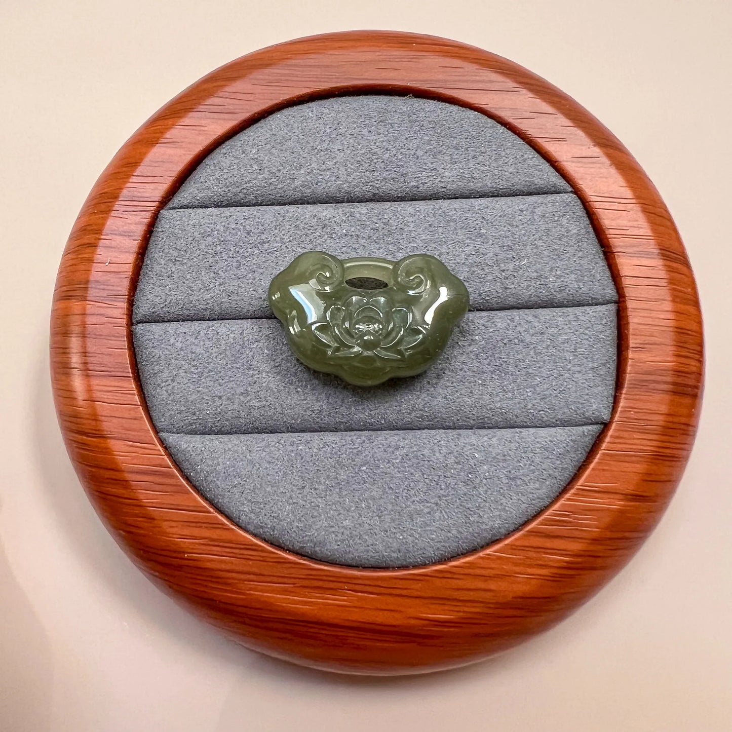 Green nephrite jade lotus ruyi pendant with glossy carved finish, displayed on gray velvet in a wooden case