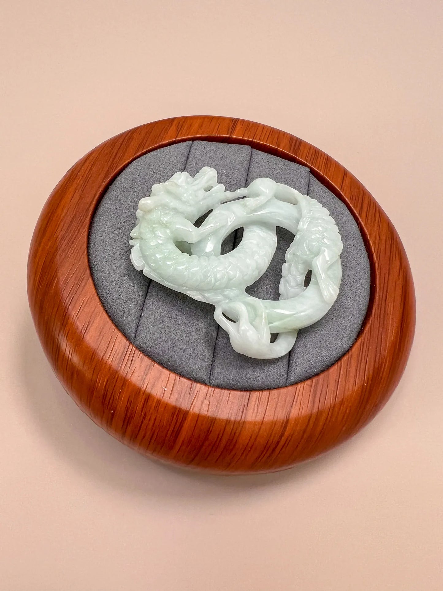 Hand-carved pale green jadeite dragon pendant on a round wooden display, top view, glossy polished finish