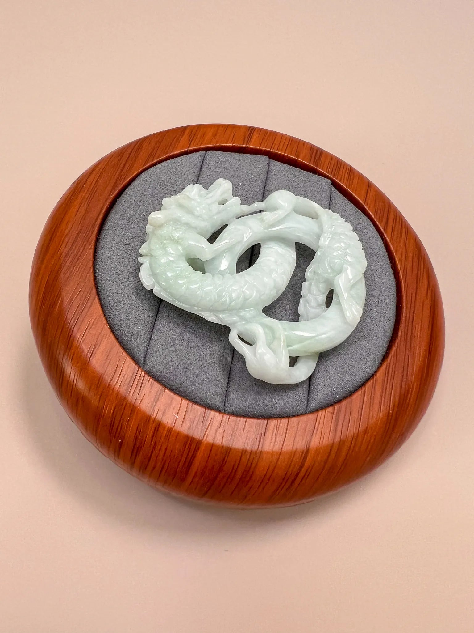 Hand-carved pale green jadeite dragon pendant on a round wooden display, top view, glossy polished finish