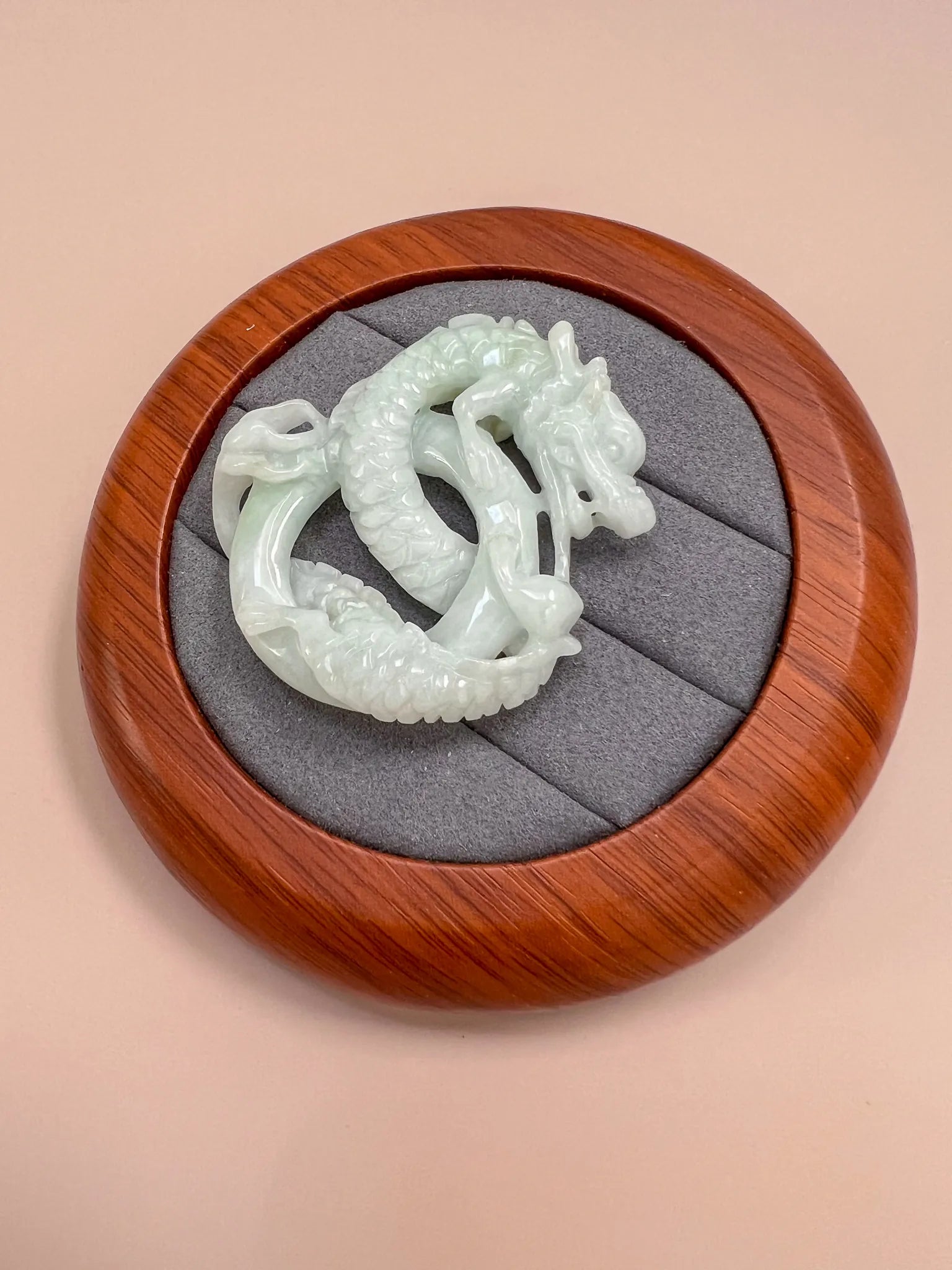 Hand-carved jadeite jade spiral dragon pendant in a round wooden display box, glossy pale green finish, top view