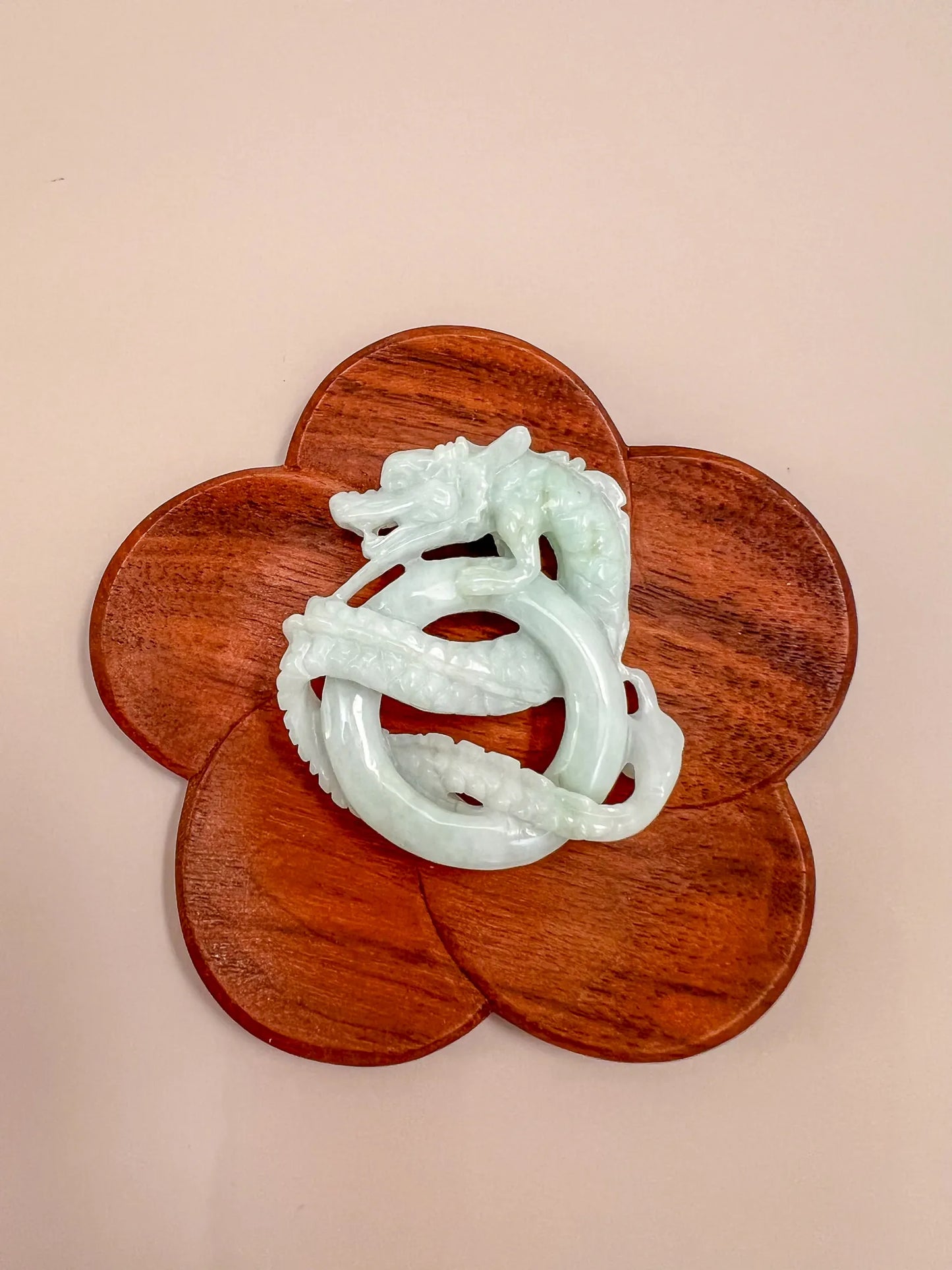 Hand-carved jadeite jade spiral dragon pendant on a wooden display, glossy pale green finish, close-up angle