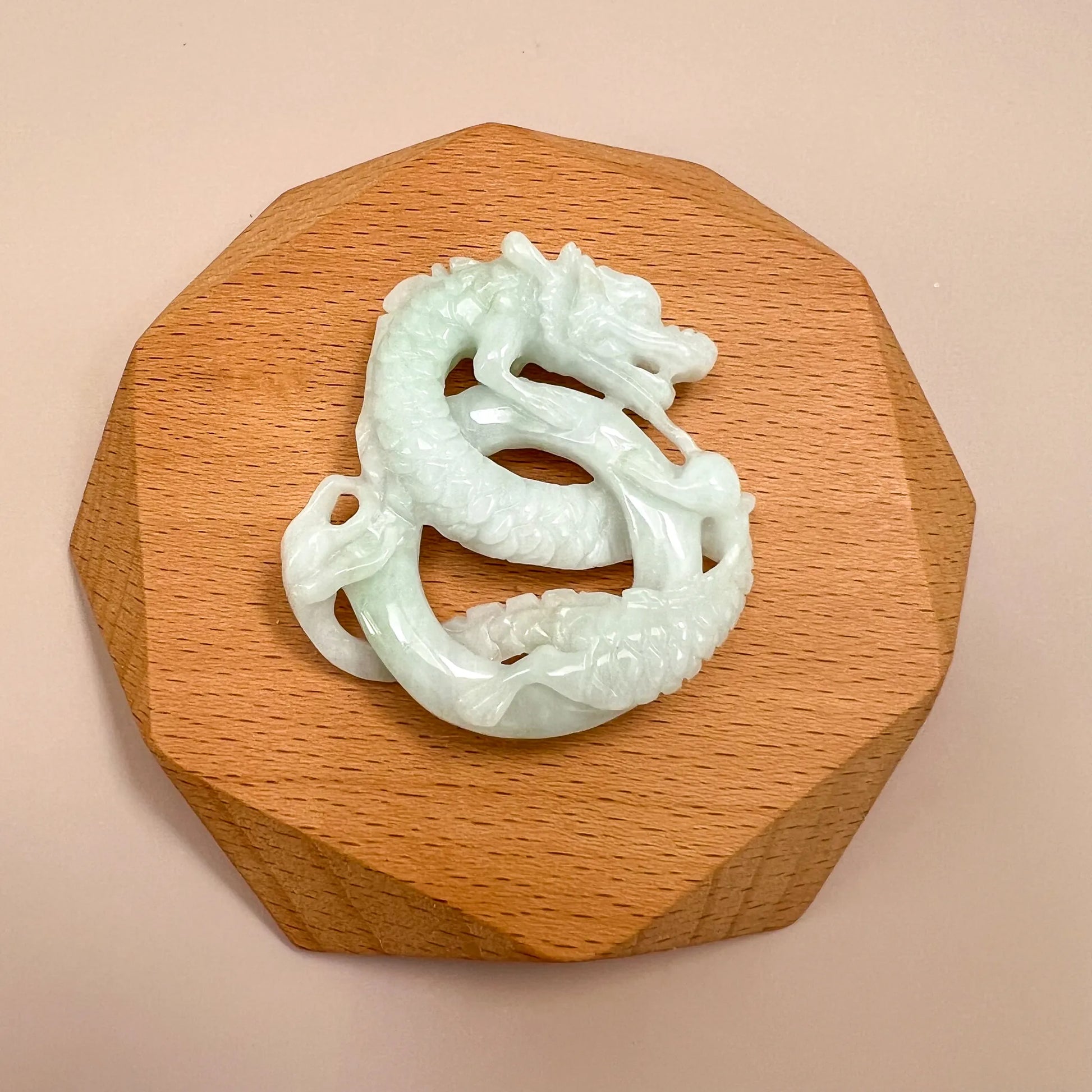 Hand-carved jadeite jade spiral dragon pendant, glossy pale green-white, shown on a wooden display stand, top view