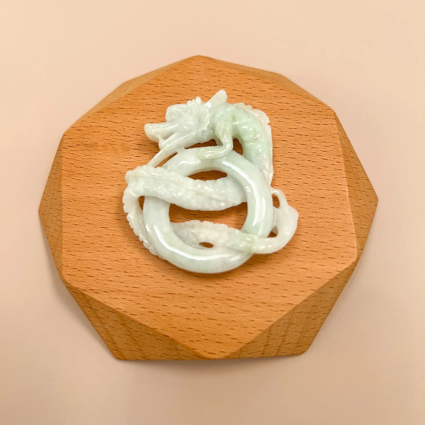 Hand-carved jadeite dragon pendant on wooden stand, glossy pale green-white stone, top-down view