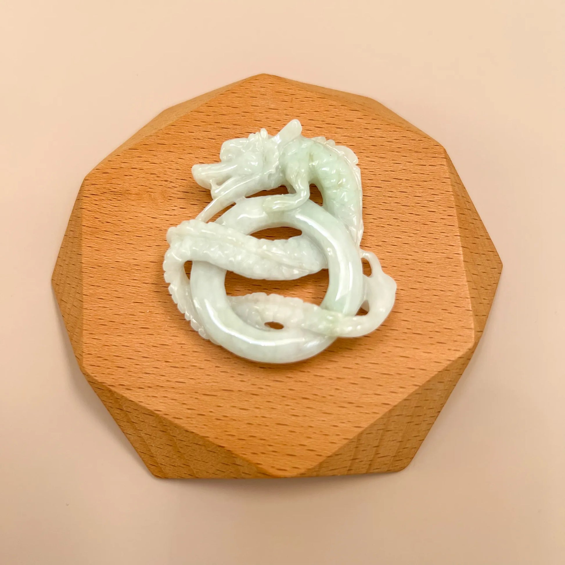 Hand-carved jadeite dragon pendant on wooden stand, glossy pale green-white stone, top-down view