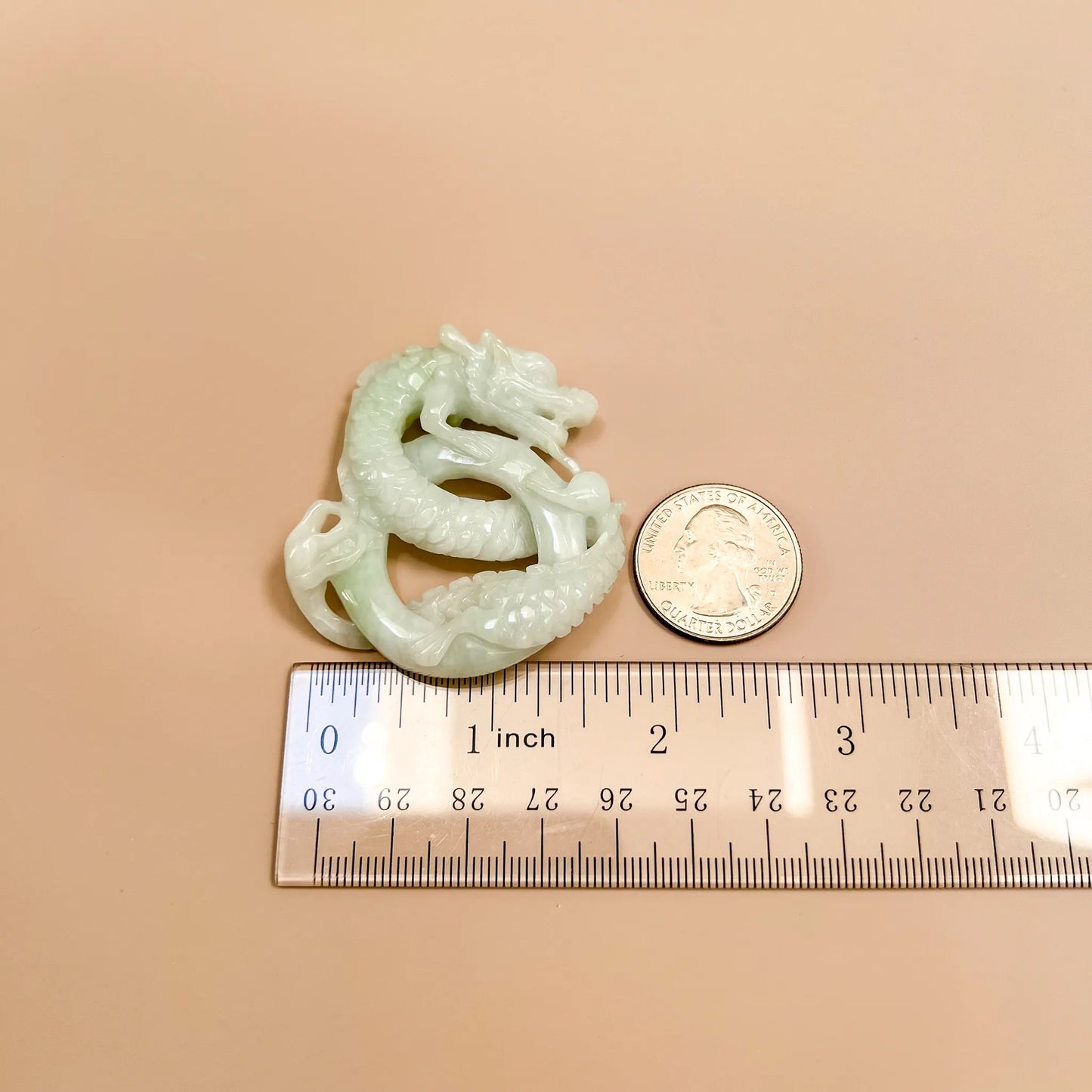 Hand-carved jadeite dragon pendant, side view with glossy pale green finish, shown beside quarter and ruler for scale