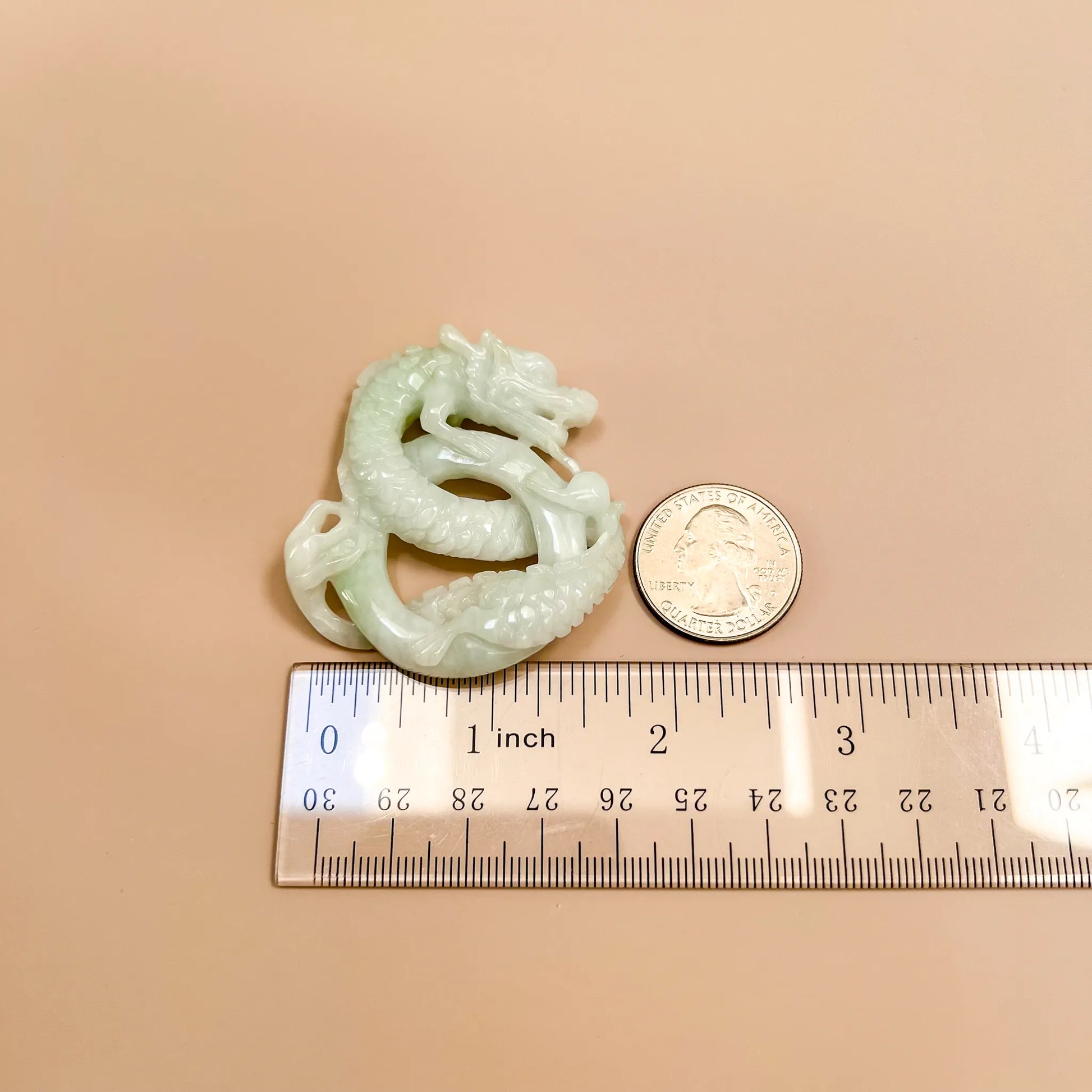 Hand-carved jadeite dragon pendant, side view with glossy pale green finish, shown beside quarter and ruler for scale