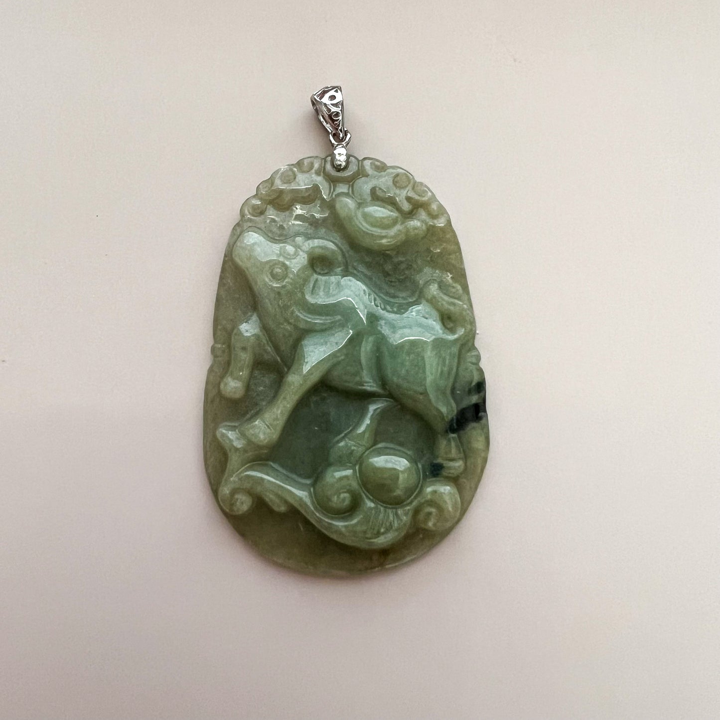 Close-up front view of carved green jadeite ox pendant with glossy finish and sterling silver bail