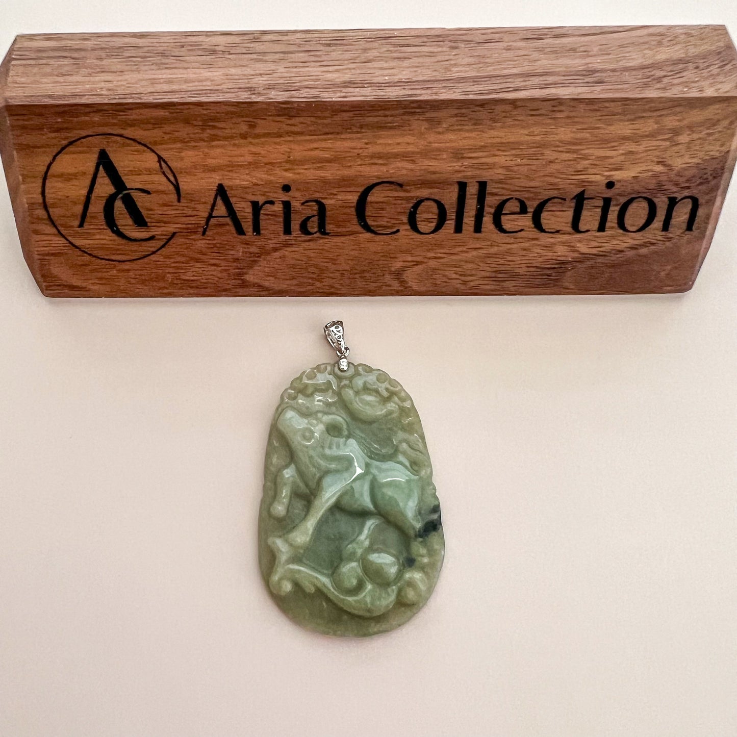 Green jadeite pendant with ox and ruyi carving, glossy textured finish, sterling silver bail, shown on display card