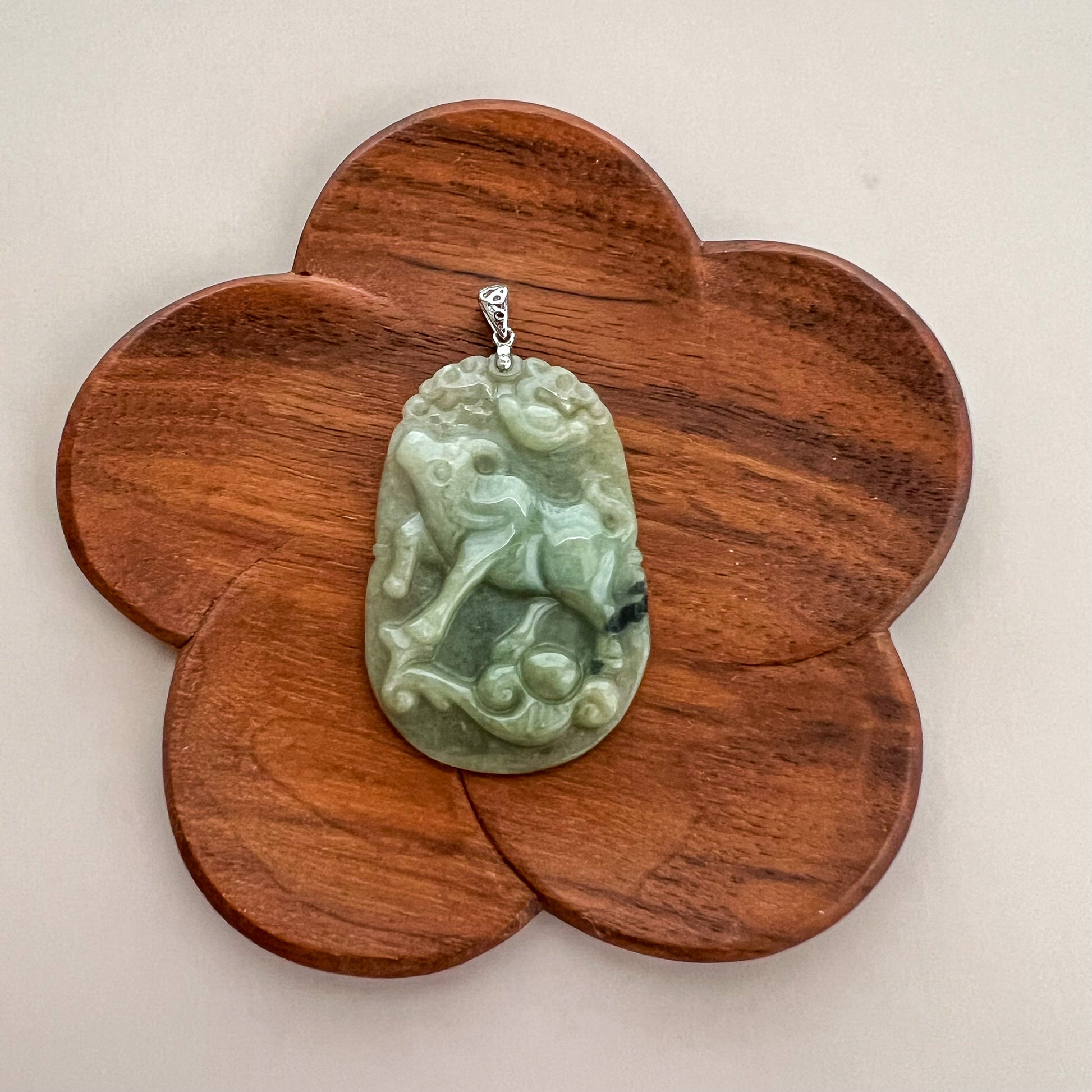 Green jadeite ox and ruyi pendant with sterling silver bail, polished carved finish on wooden display