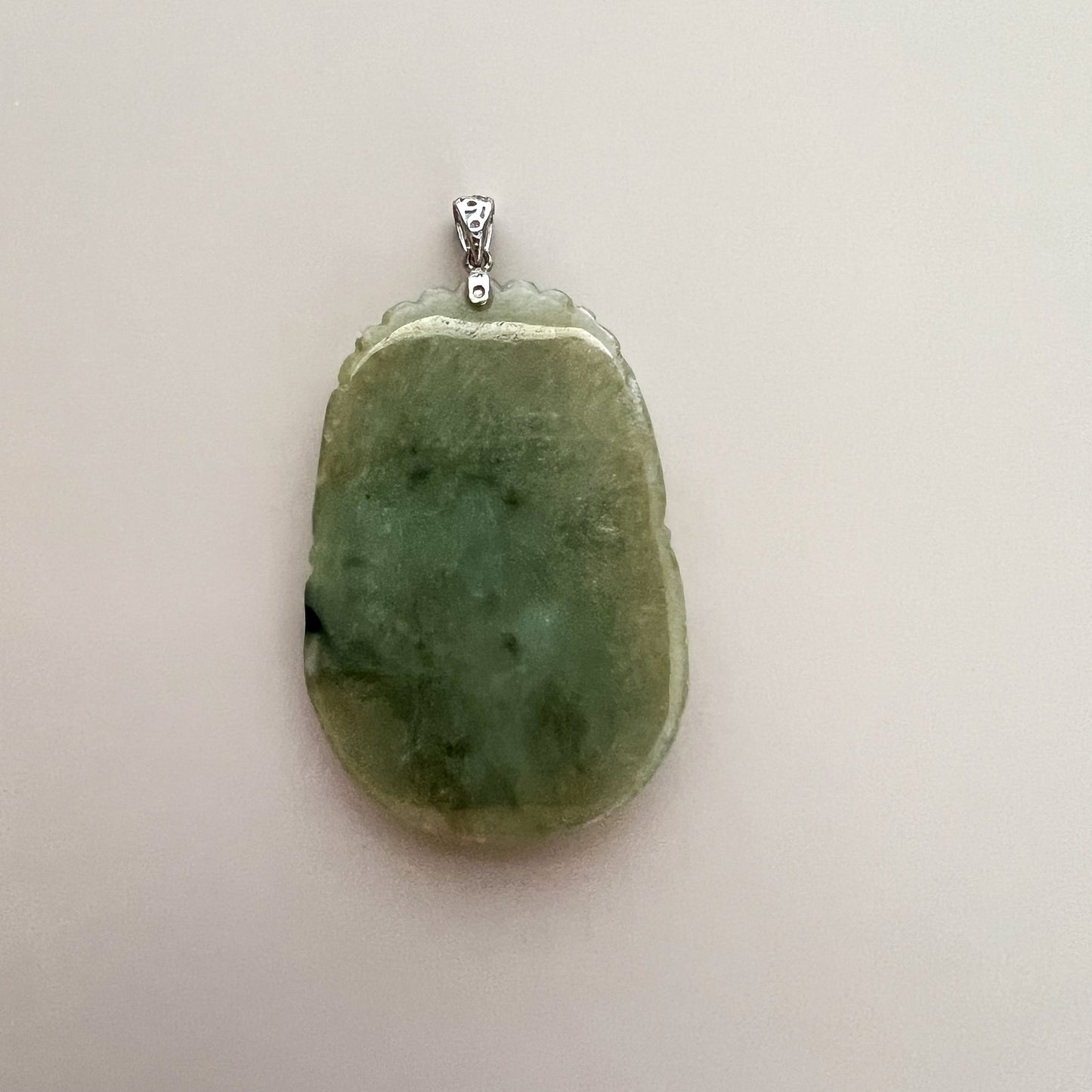 Close-up back view of green jadeite pendant with sterling silver bail, polished textured stone on white background