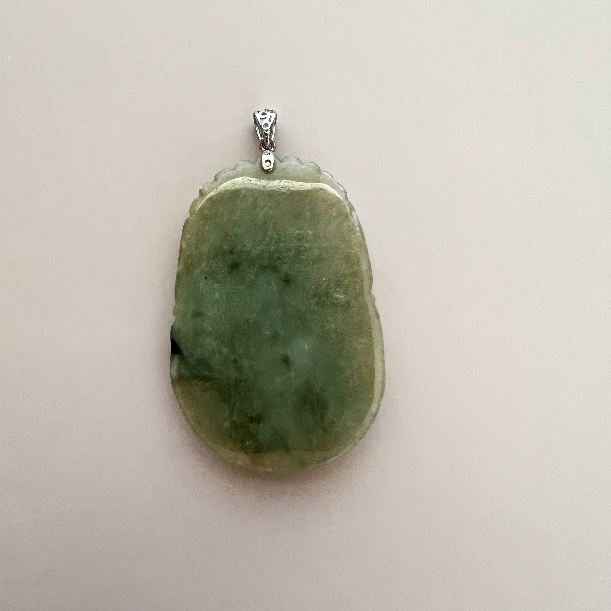 Close-up back view of green jadeite pendant with sterling silver bail, polished textured stone on white background