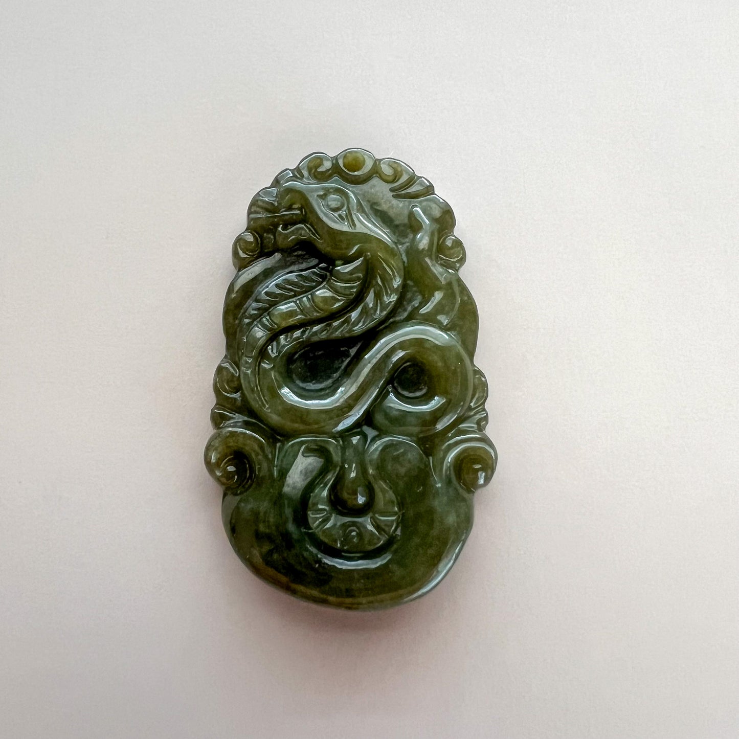 Close-up of carved green jadeite jade zodiac pendant with glossy finish and intricate relief details on white background